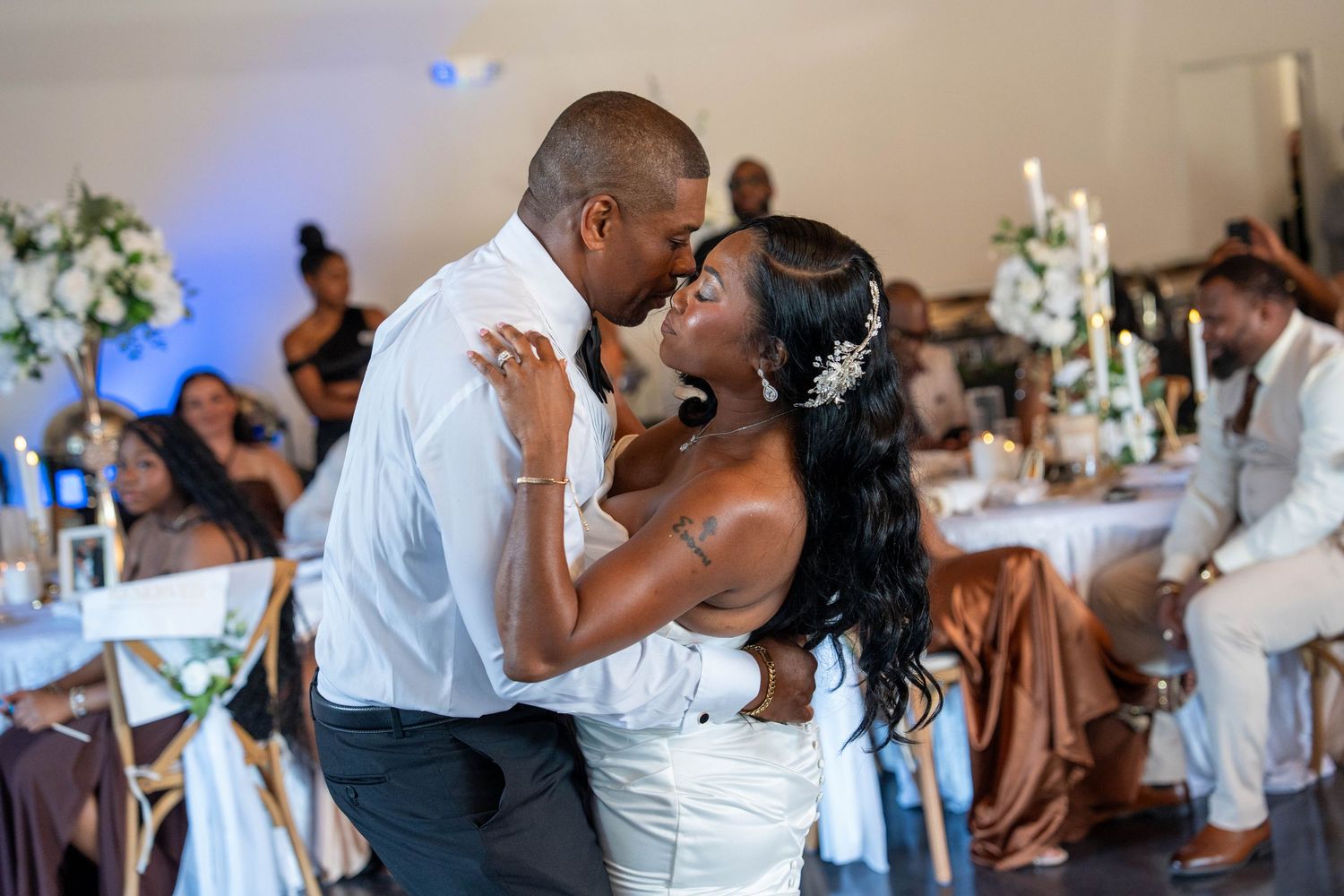 Bride and groom share their first dance at wedding reception, guests seated at decorated tables in background.
