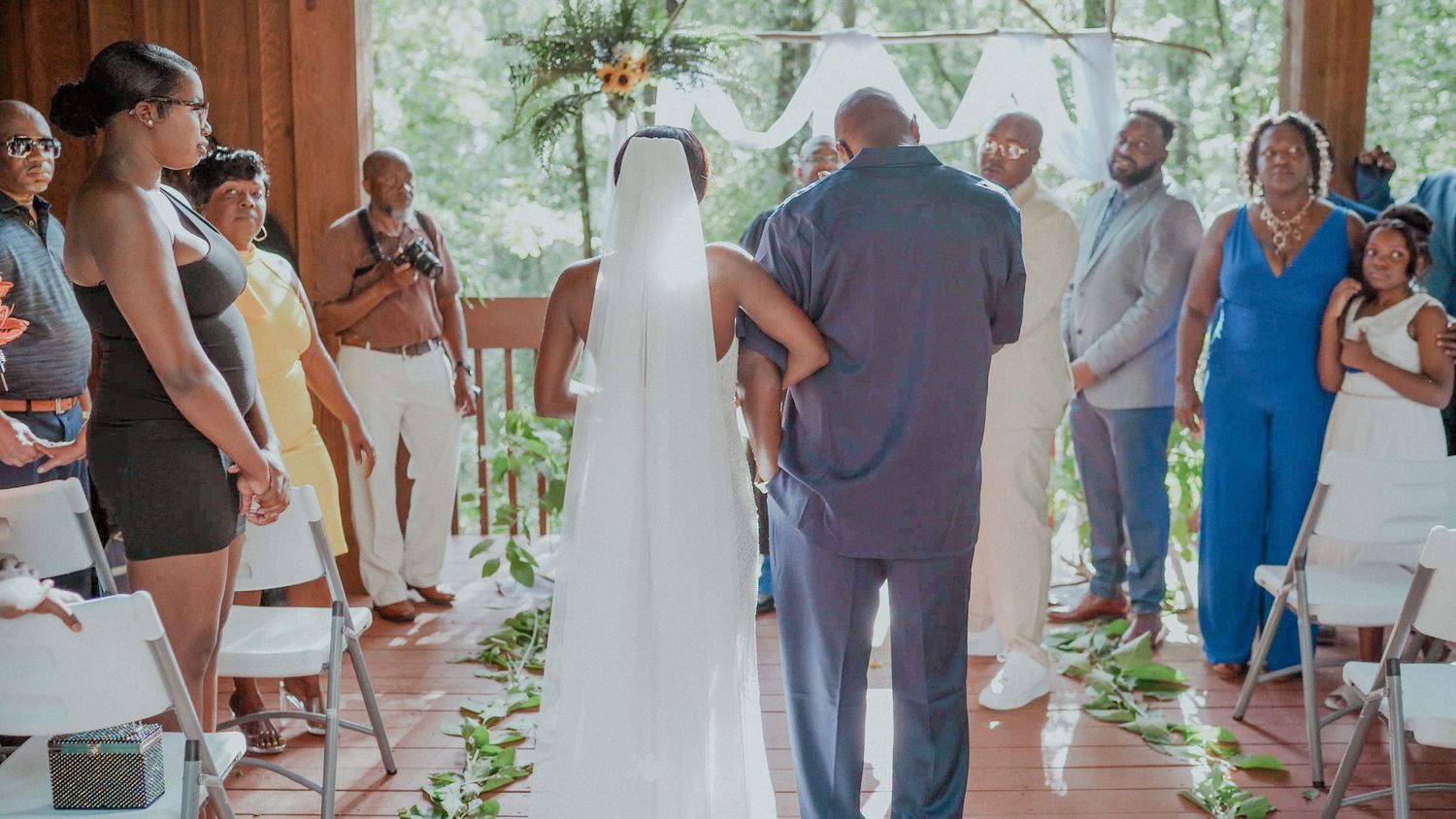 Wedding guests dance and celebrate together during a lively reception under a covered outdoor pavilion.