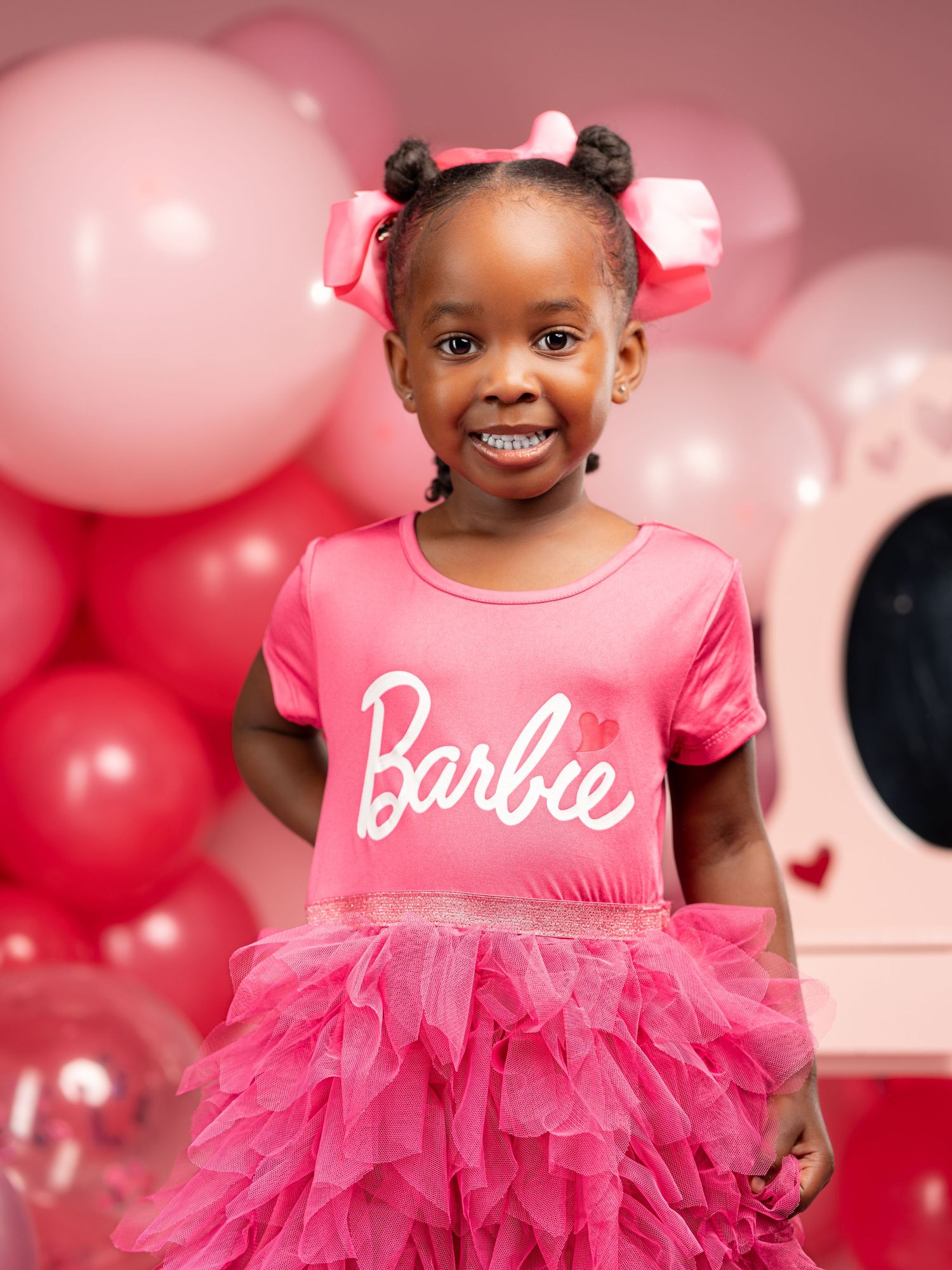 Festive pink photoshoot featuring a tulle dress and Barbie branding surrounded by pink and silver balloons.