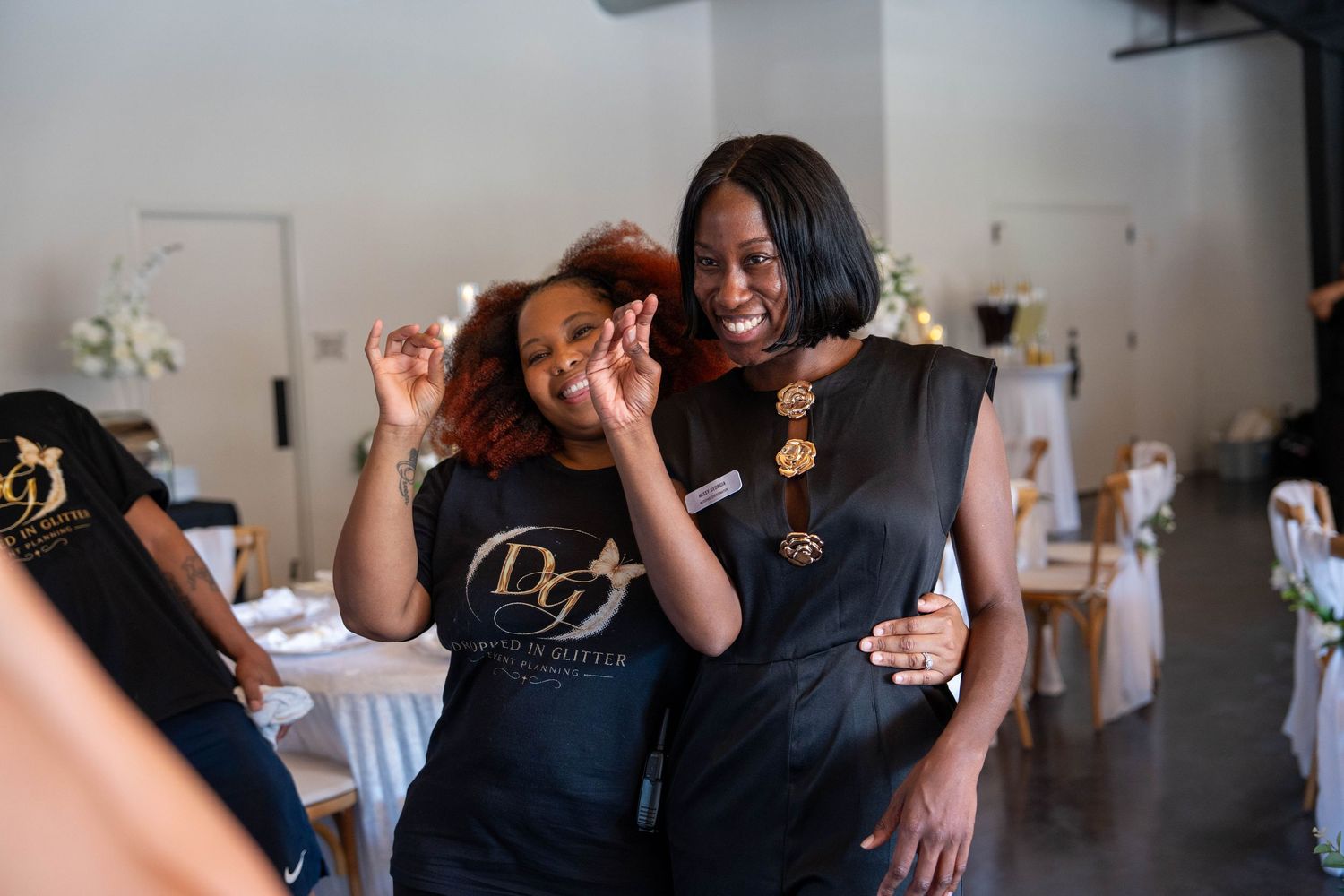 Two women in black event staff uniforms smiling and posing together at a wedding reception venue.