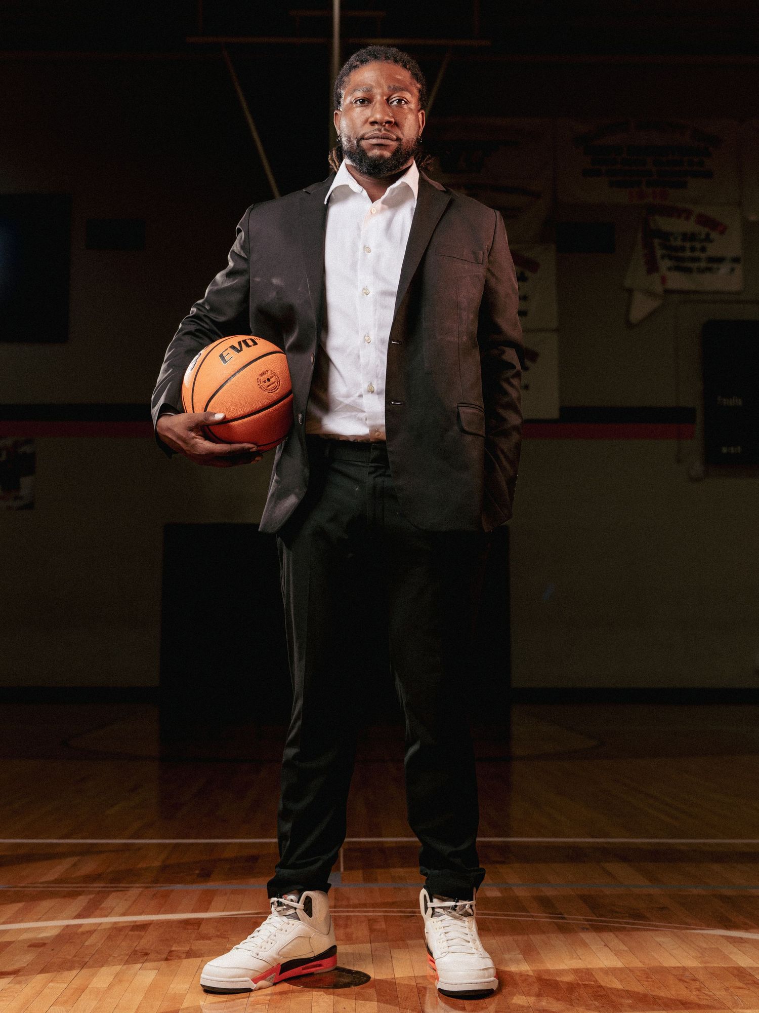 Basketball player in formal attire poses with ball in gymnasium setting in series of connected photos.