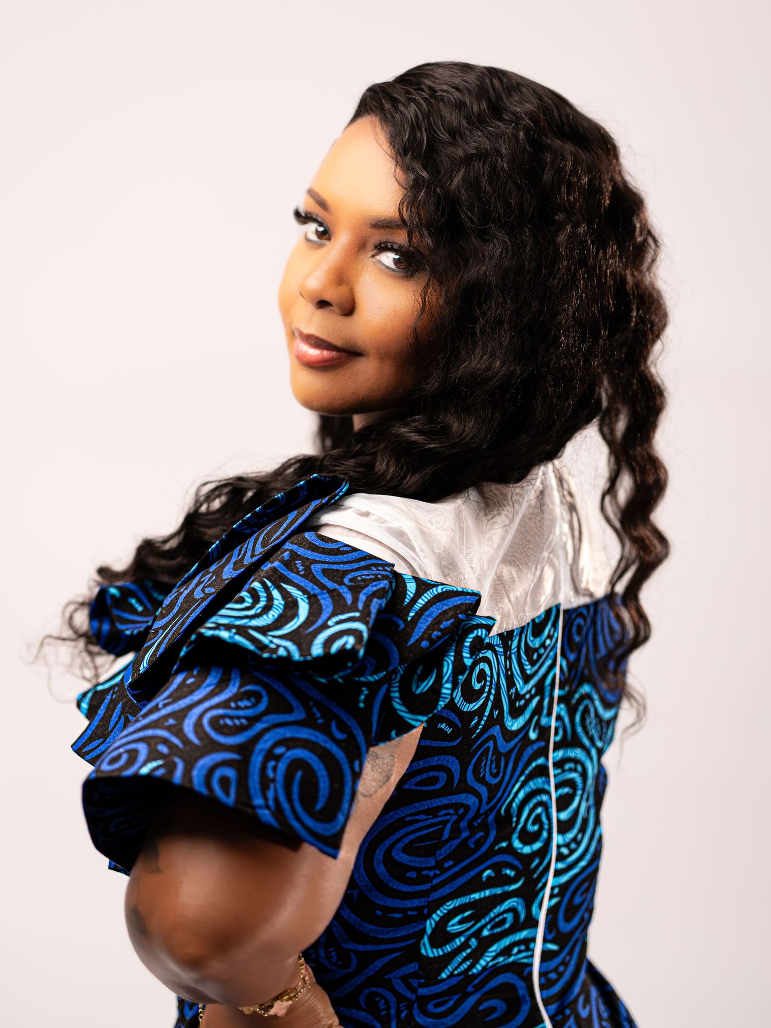 Portrait against light background wearing a blue and black patterned dress with wavy dark hair styled elegantly.