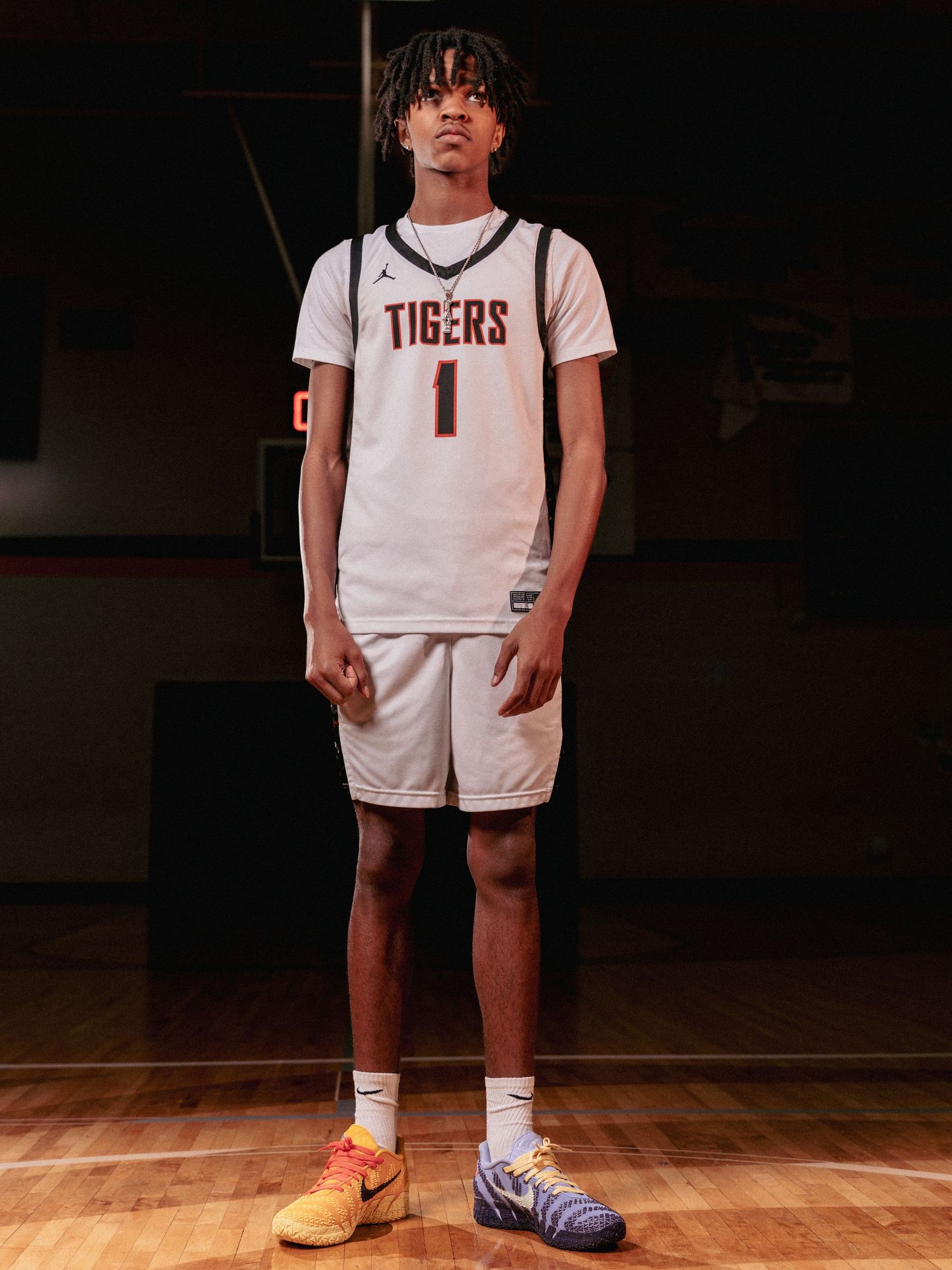 Basketball player in Tigers uniform stands on hardwood court wearing mismatched orange and blue sneakers.