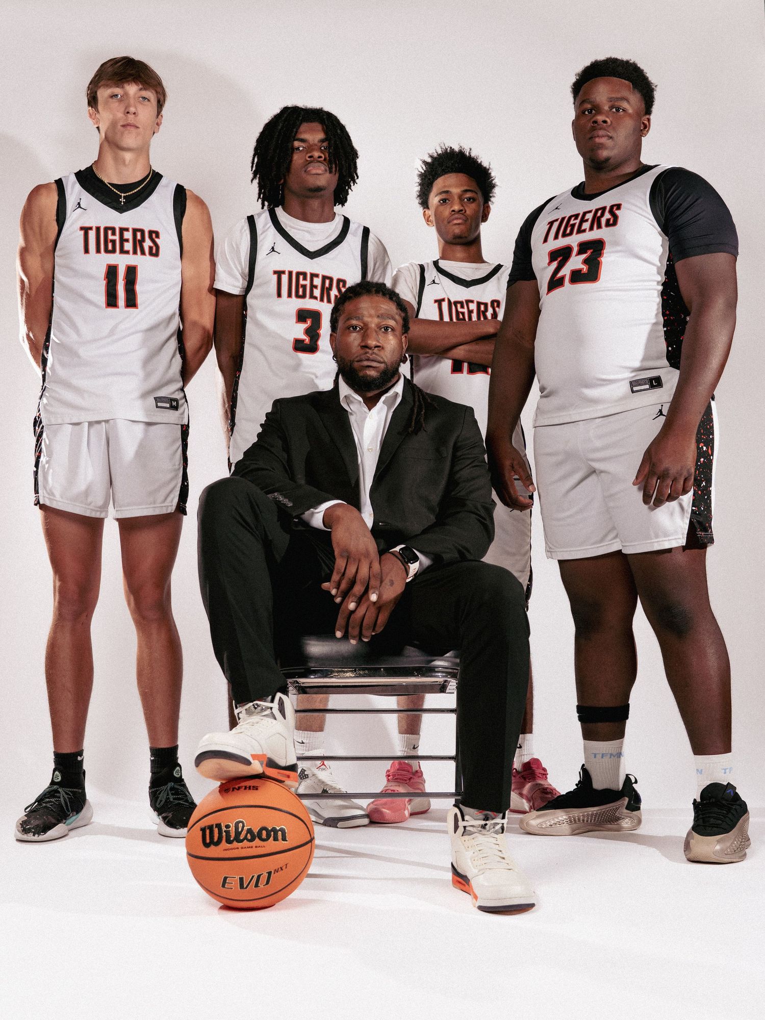 Basketball team members pose together in white Tigers uniforms with Wilson basketball.