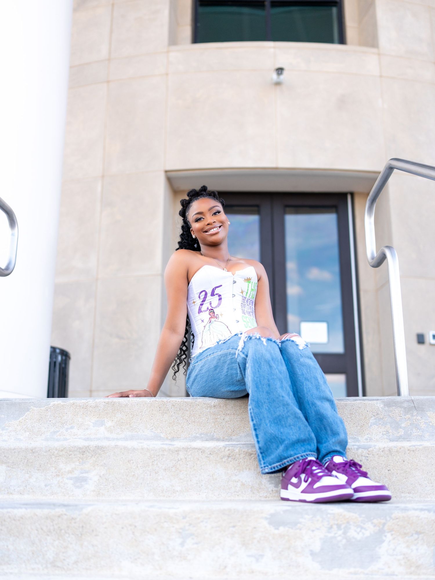 A person wearing jeans and purple sneakers sits casually on light-colored stone steps in an outdoor setting.