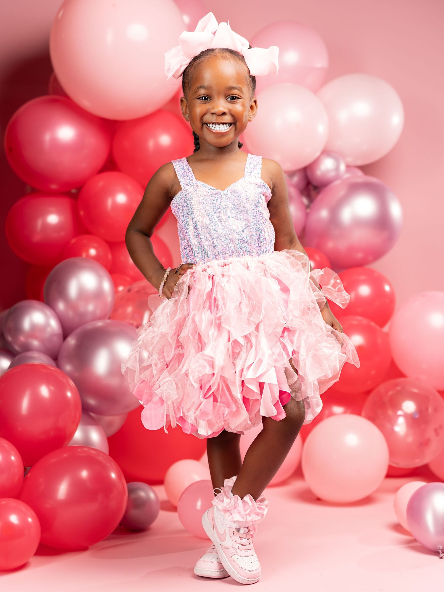 A joyful celebration scene with pink and silver balloons and a white tulle dress against a rosy backdrop.