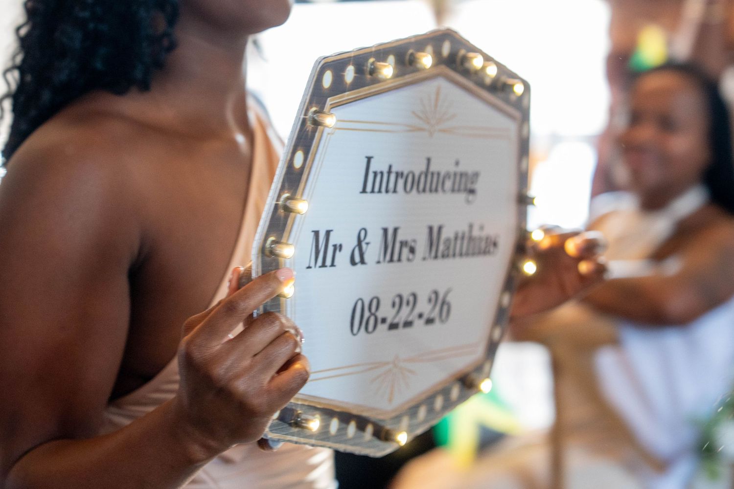 Bride holding illuminated octagonal sign introducing Mr & Mrs Matthias on 08-22-26 at wedding reception.