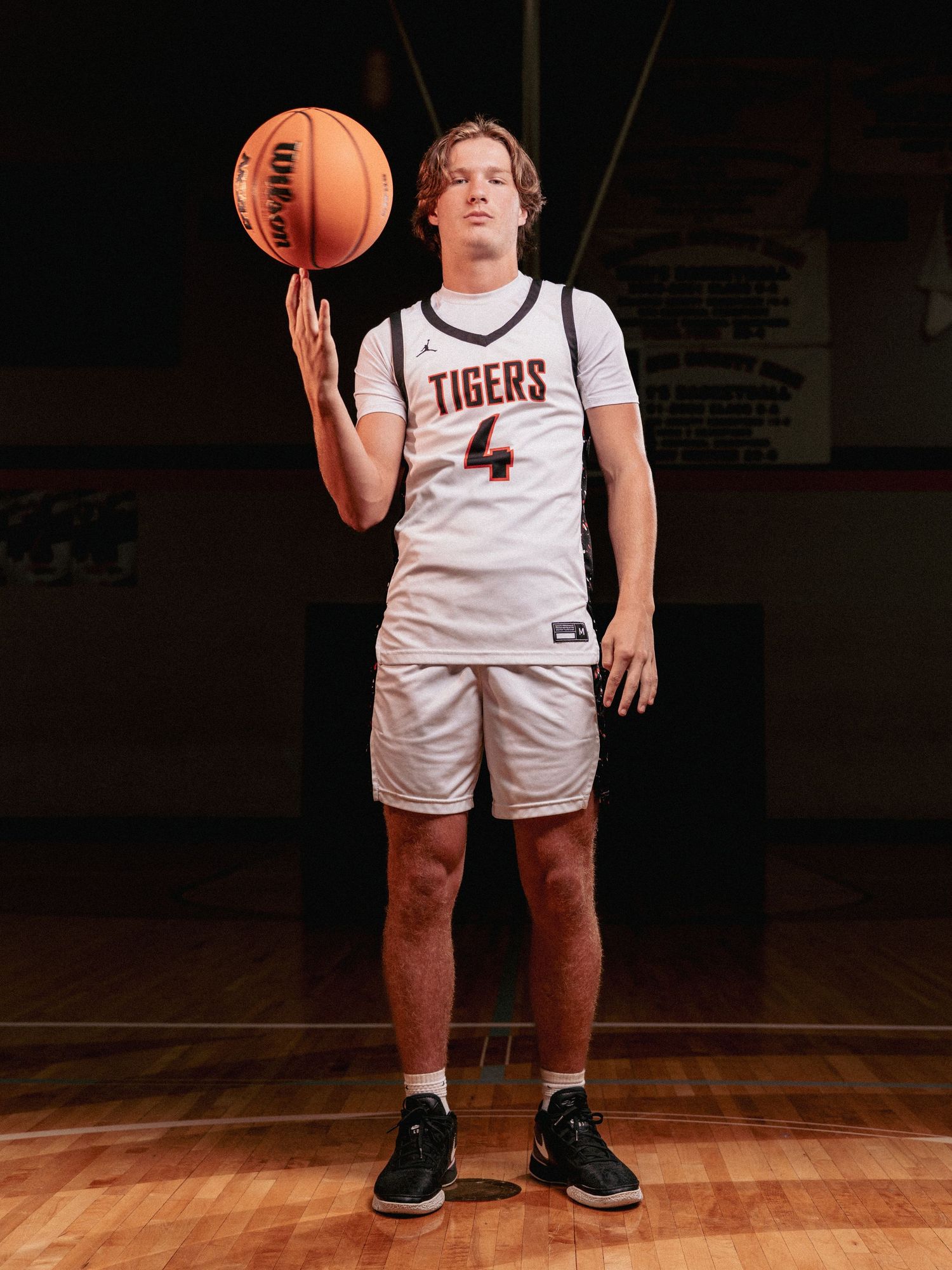 Basketball player in white Tigers uniform stands on wooden court holding ball.