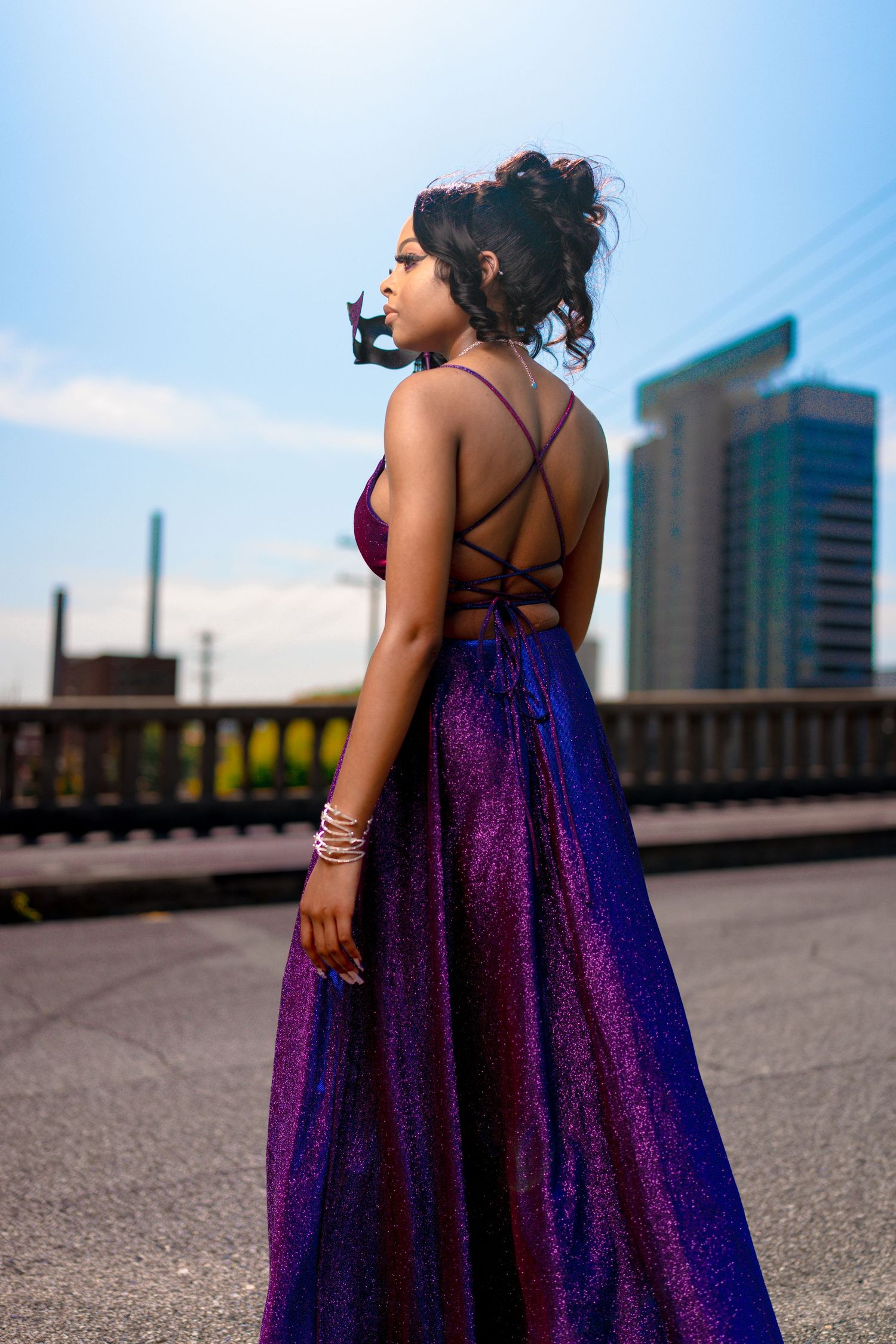 Stunning purple sparkly evening gown with strappy back detail against city backdrop.
