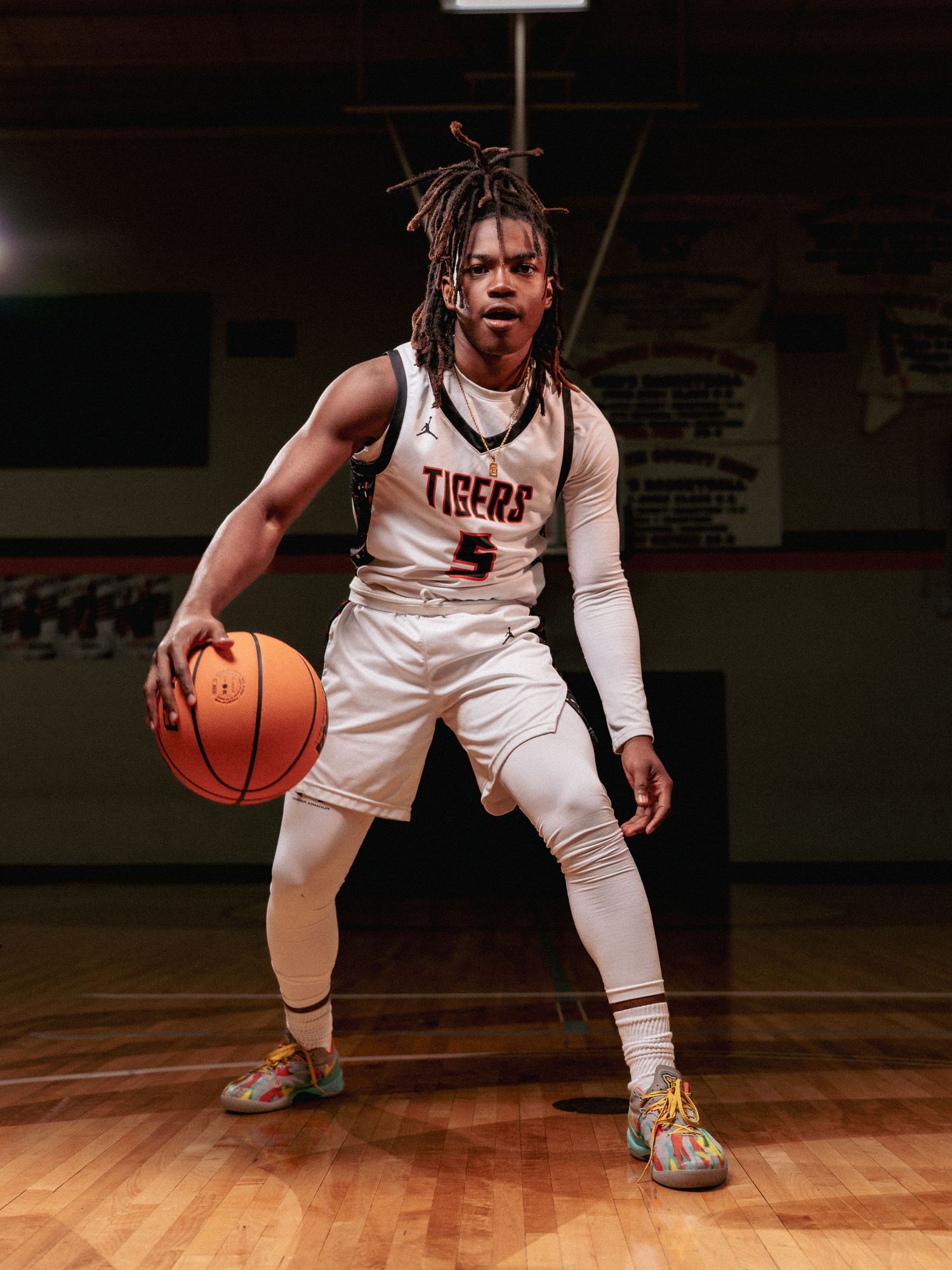Basketball player in white Tigers uniform dribbles ball in athletic stance on wooden court.