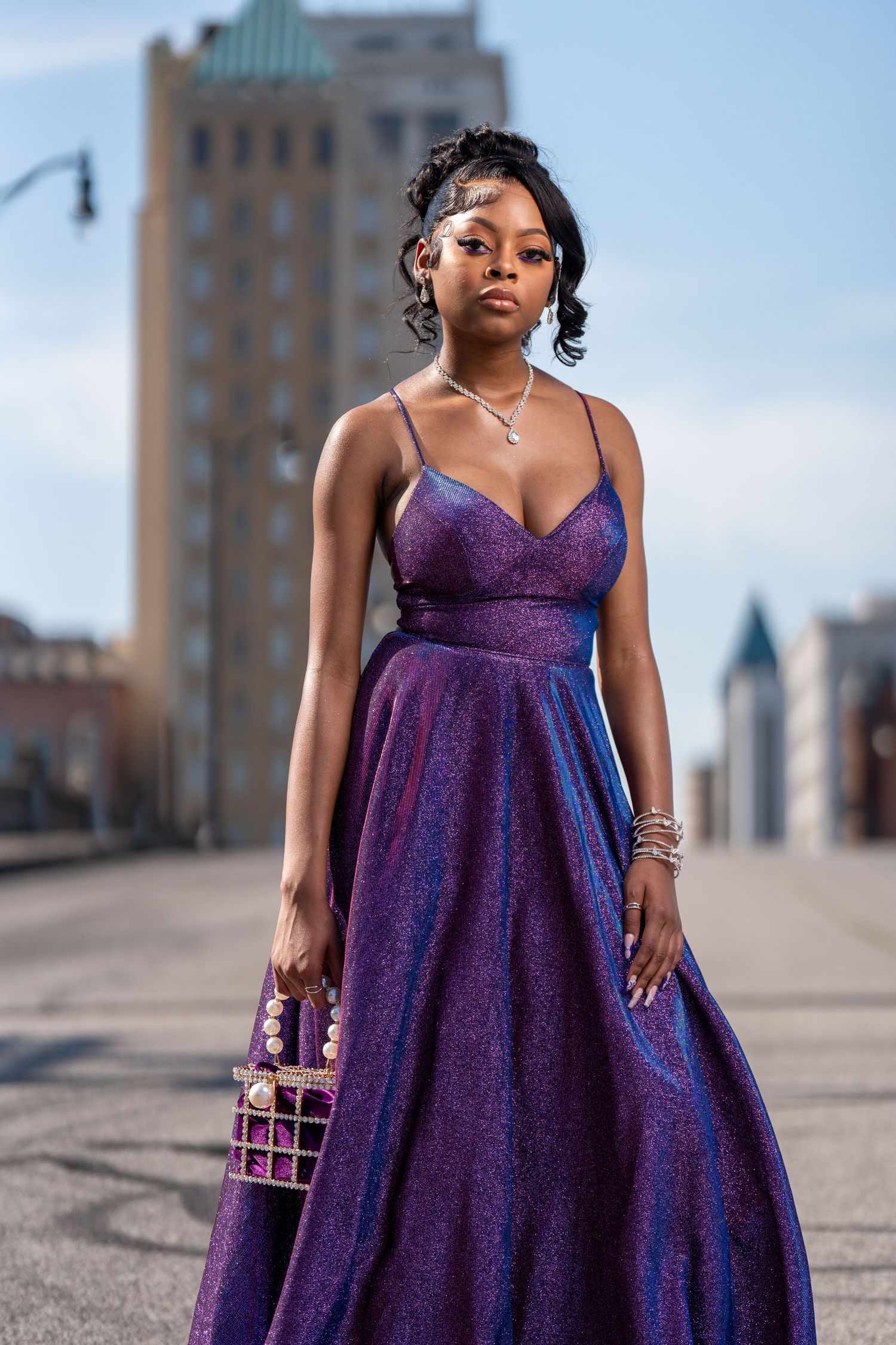 Formal purple sequin ball gown with matching purse photographed on city rooftop.