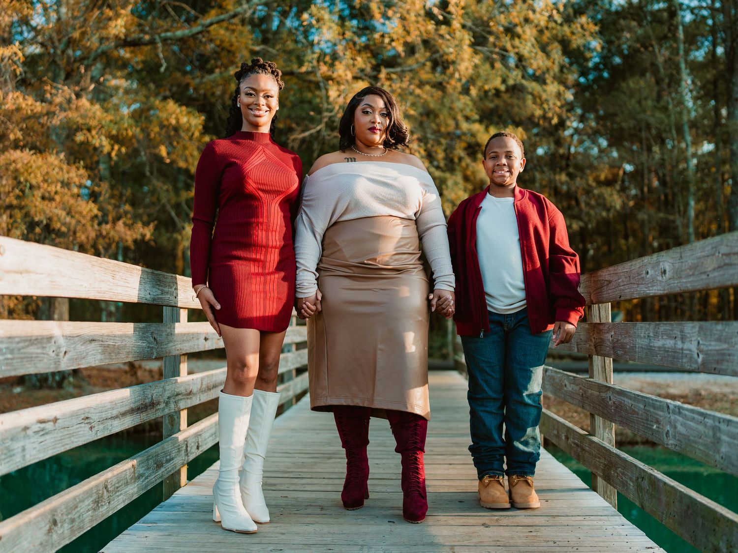 A group walks together on a wooden boardwalk surrounded by autumn foliage during a fall photo session.