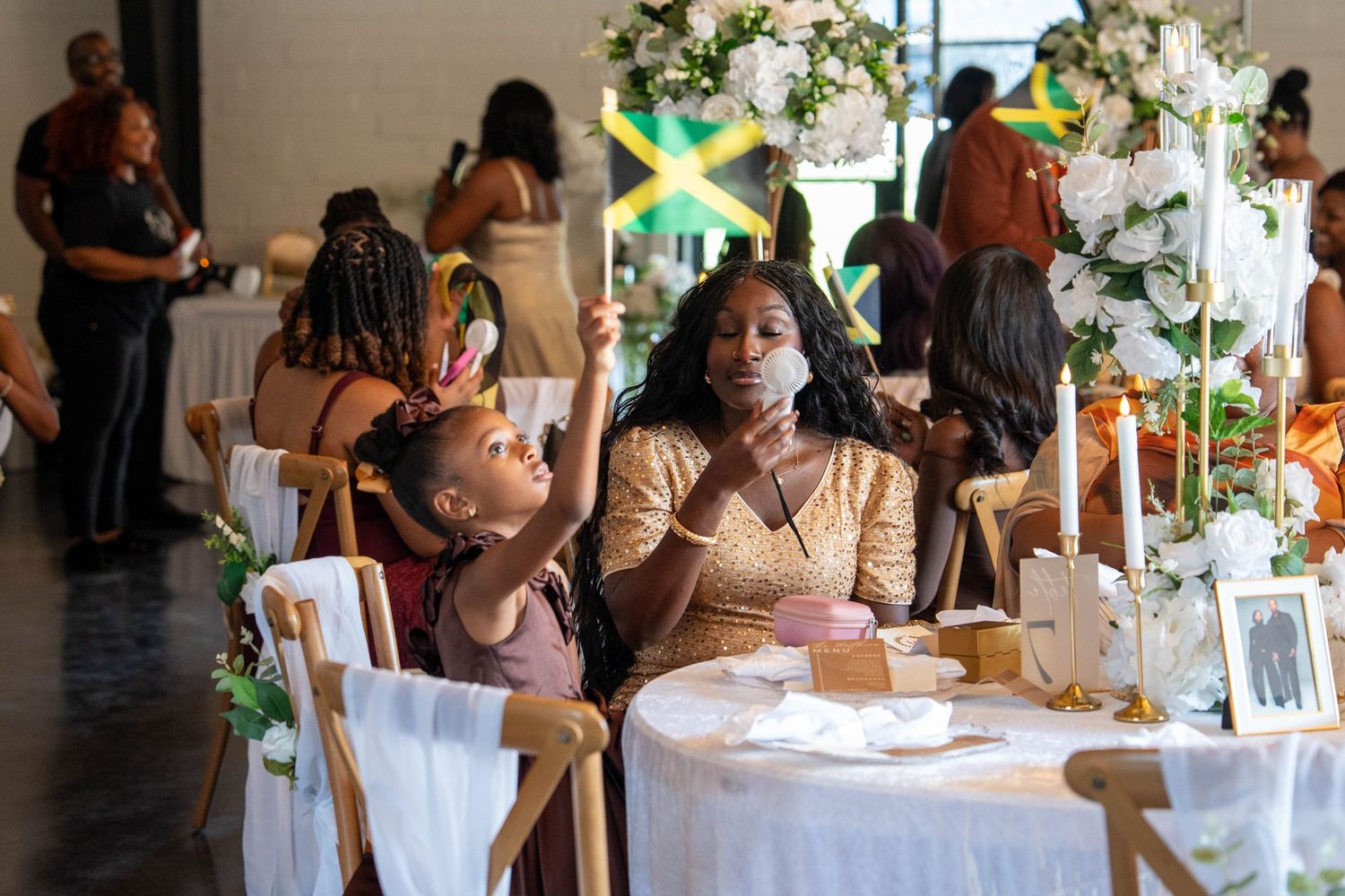 A woman and child sit at an elegant decorated table at a Jamaican celebration event with floral arrangements.
