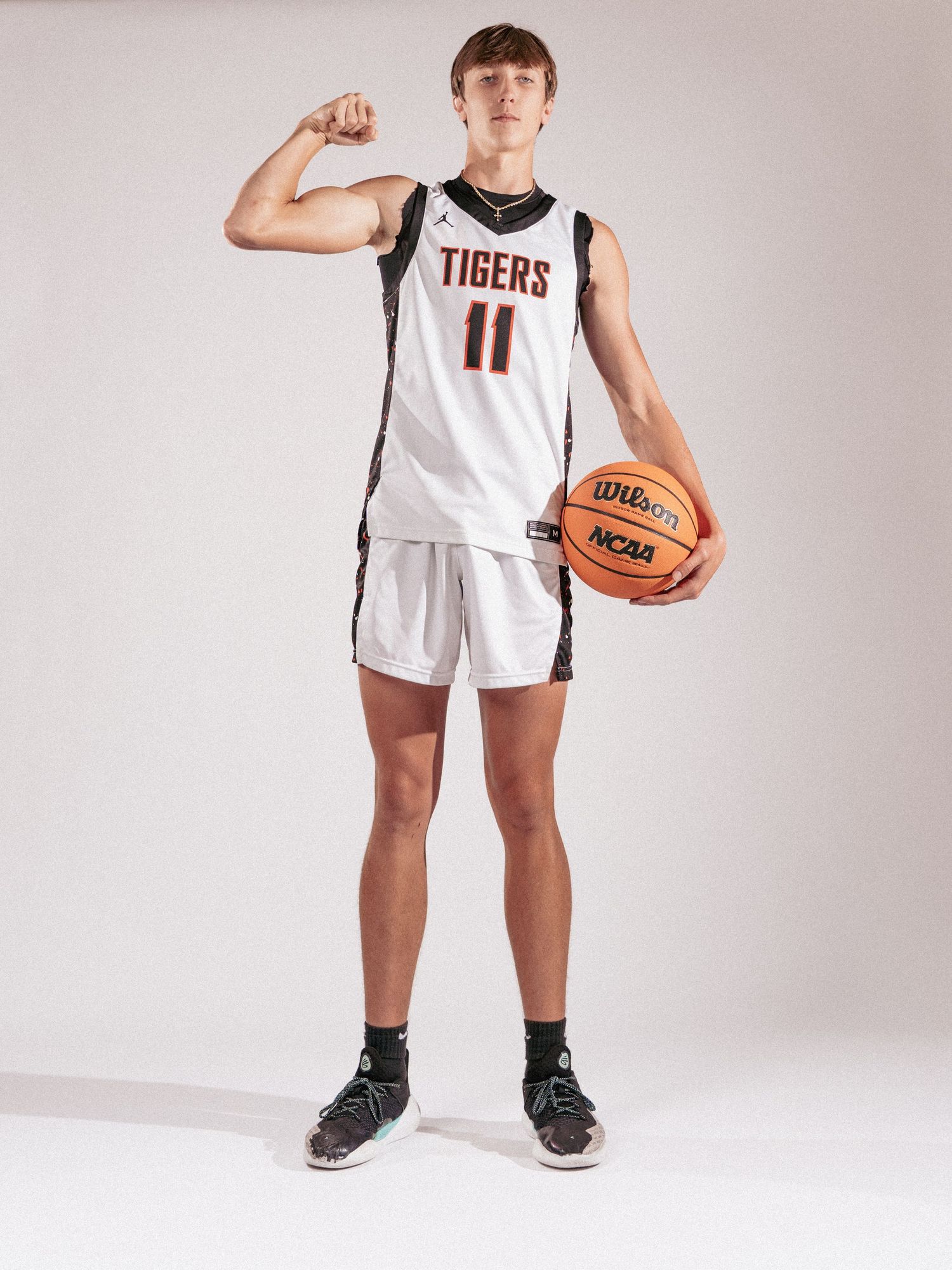 Youth basketball player in Tigers uniform poses with ball against white studio background.