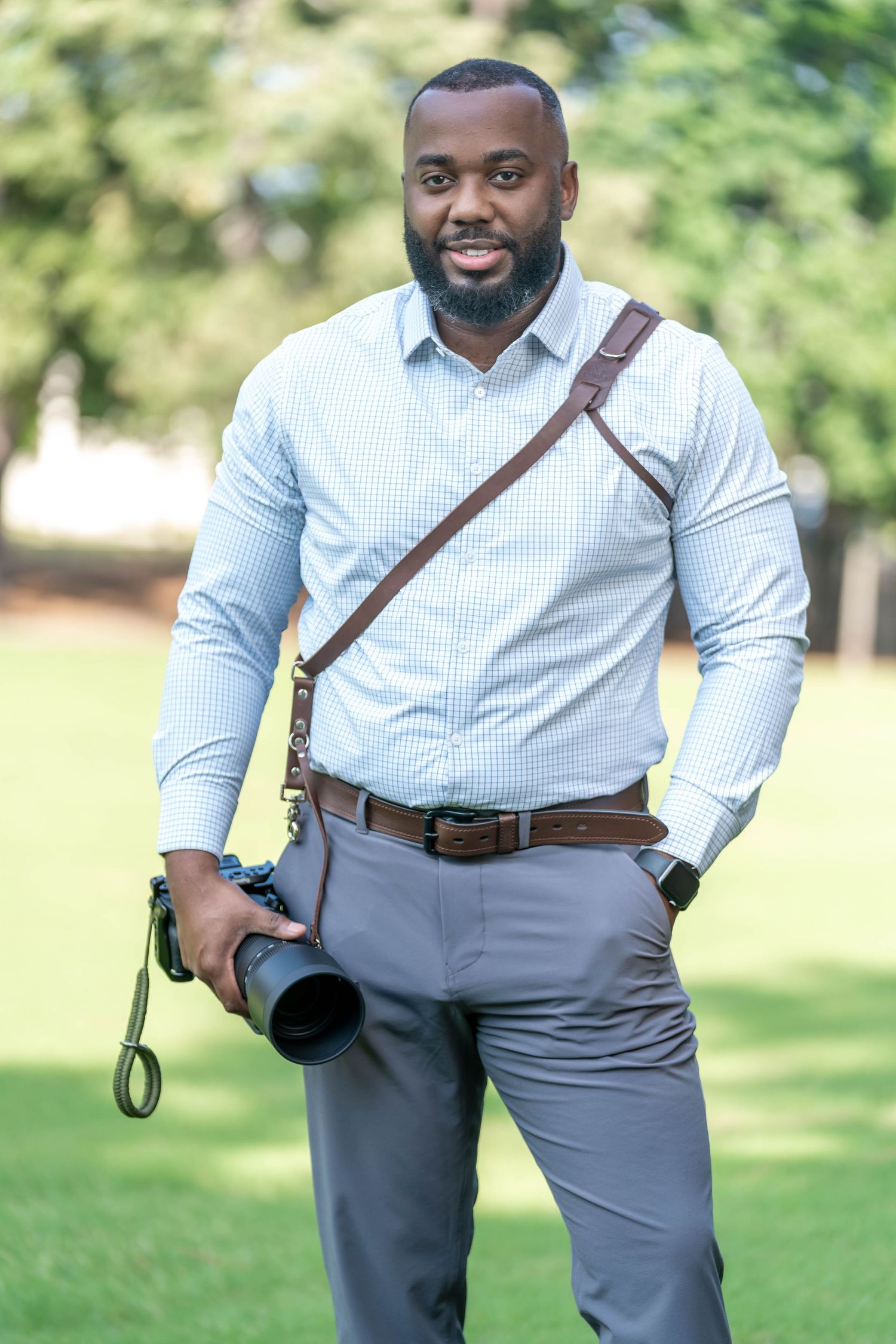 Professional photographer in light blue dress shirt and gray slacks with camera equipment outdoors.
