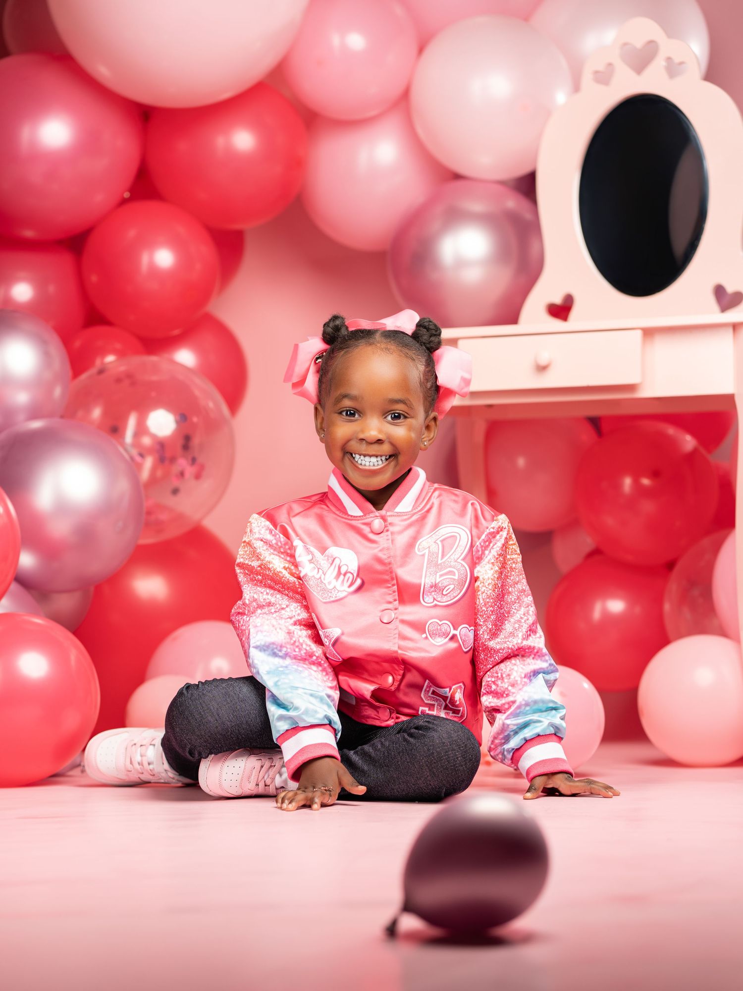 A child in pink satin lounges on the floor surrounded by red, pink and silver balloon decorations for Valentine's Day.