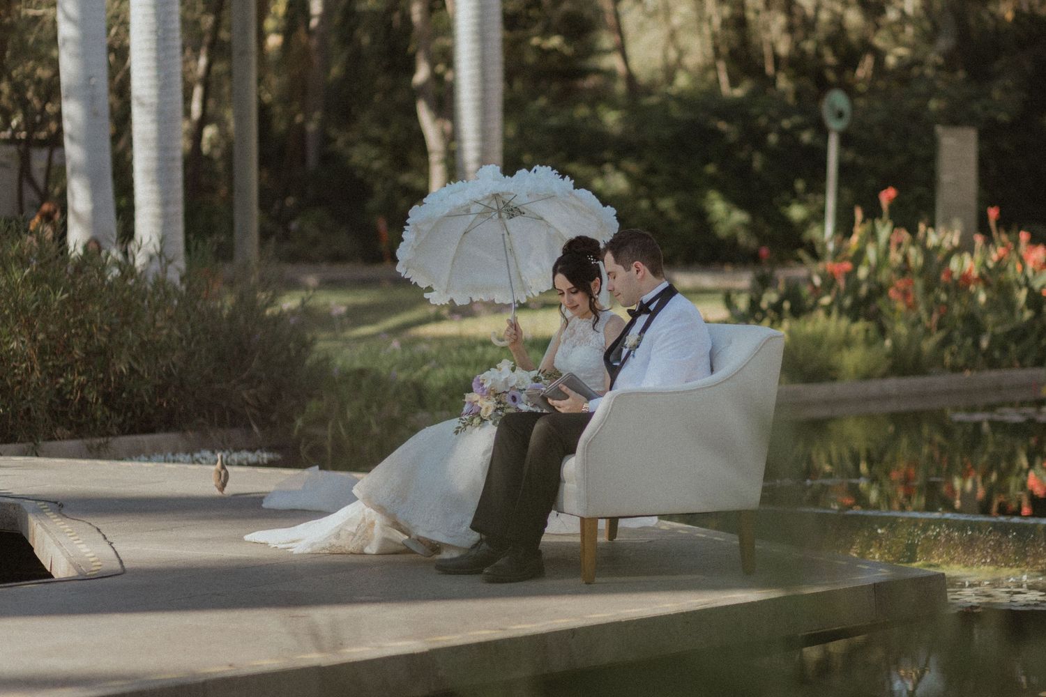 Couple relaxing on white outdoor furniture in a garden setting with a parasol.