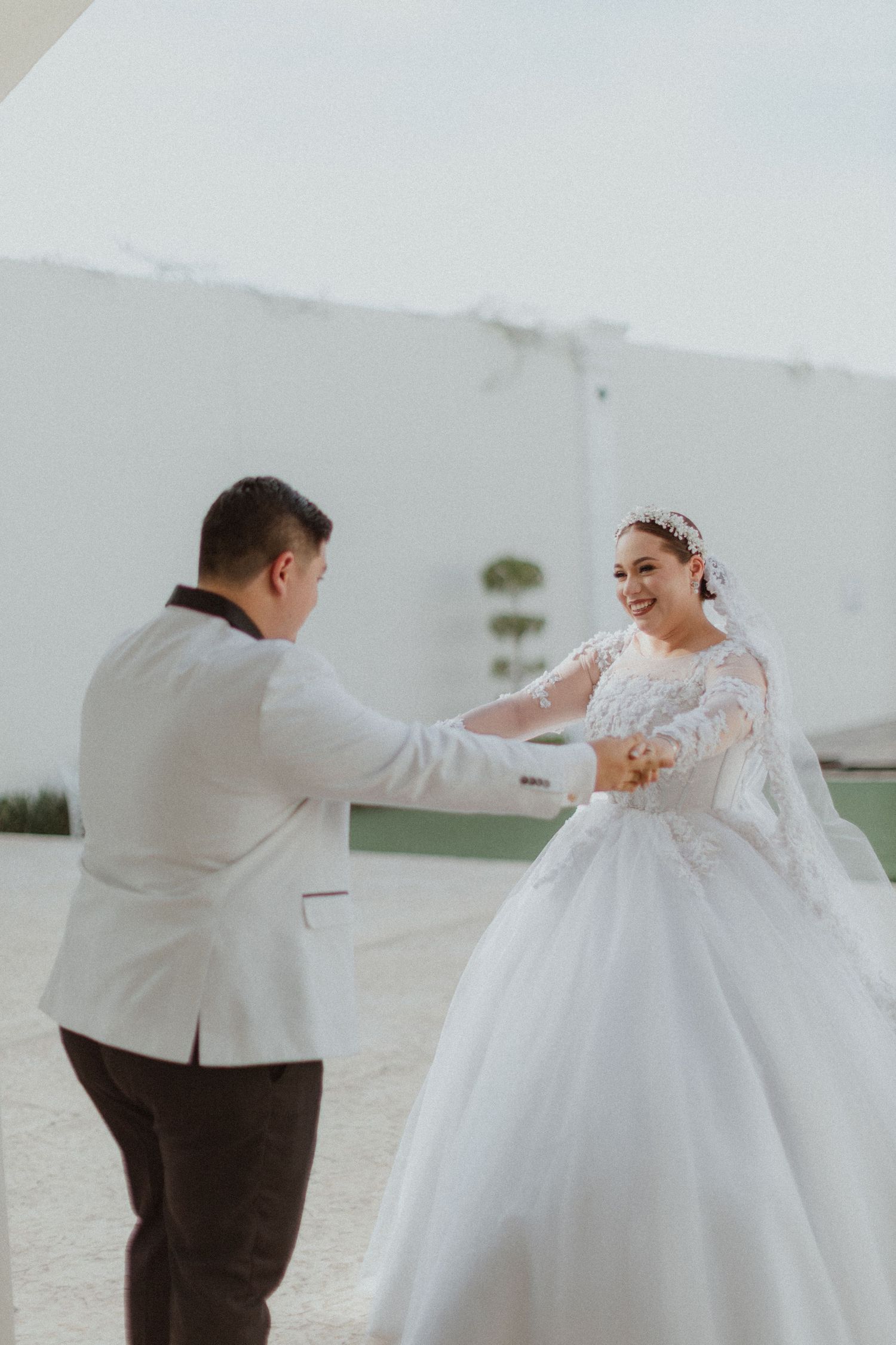 A couple dancing and laughing together in their wedding attire against a white backdrop.