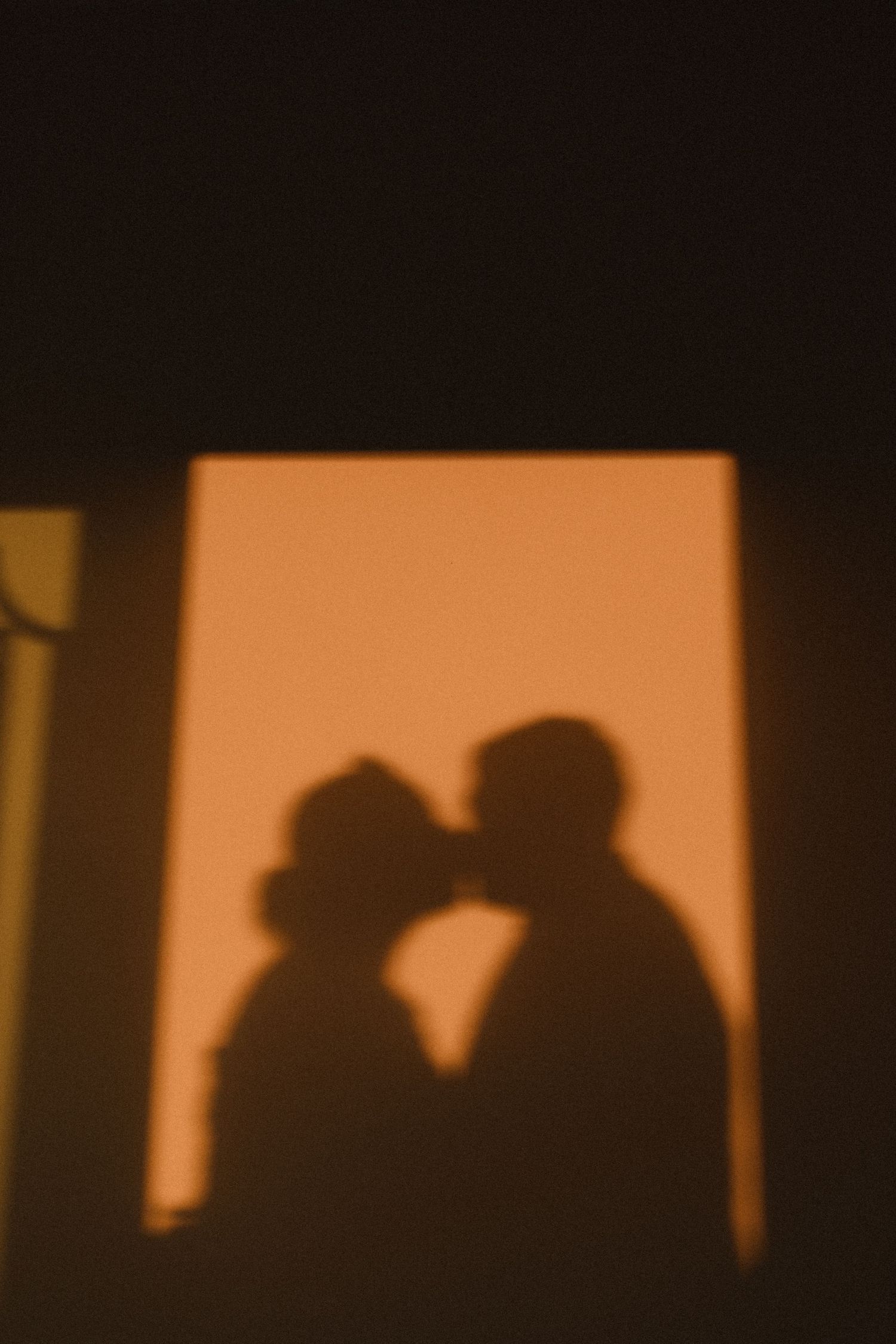 Silhouette of couple against orange backlight creating romantic shadow effect.