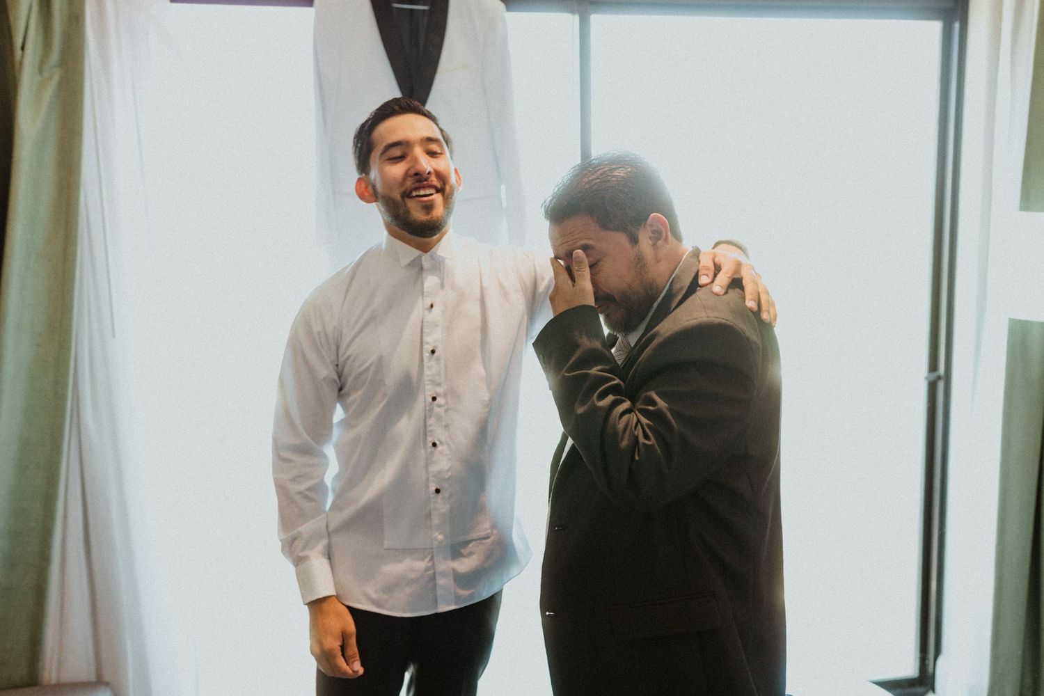 Two people in formal attire sharing an emotional moment in a bright room.