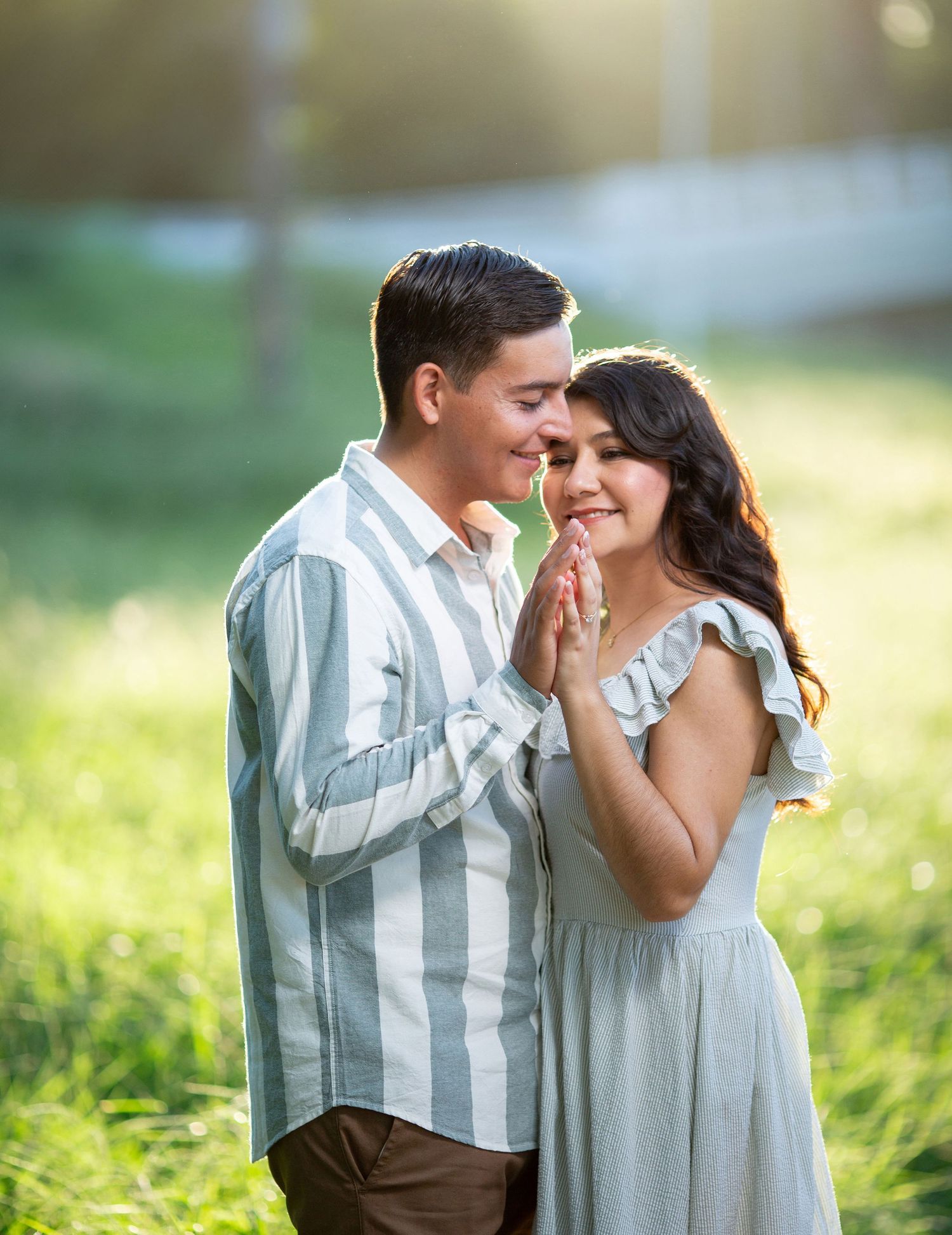 A couple in light summer clothing sharing an intimate moment in a sunlit meadow.