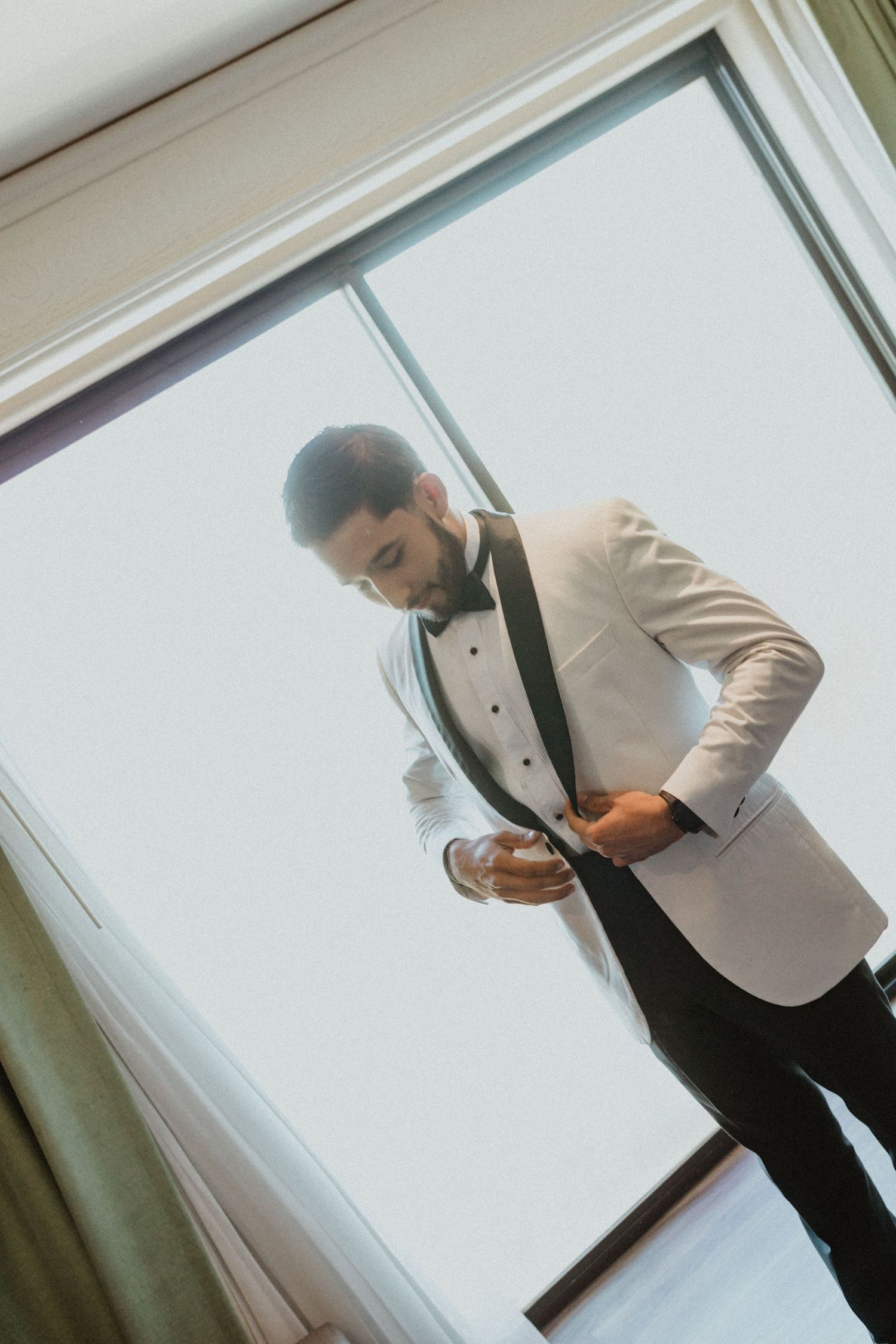 Person in a light colored tuxedo jacket and bowtie adjusting their outfit.