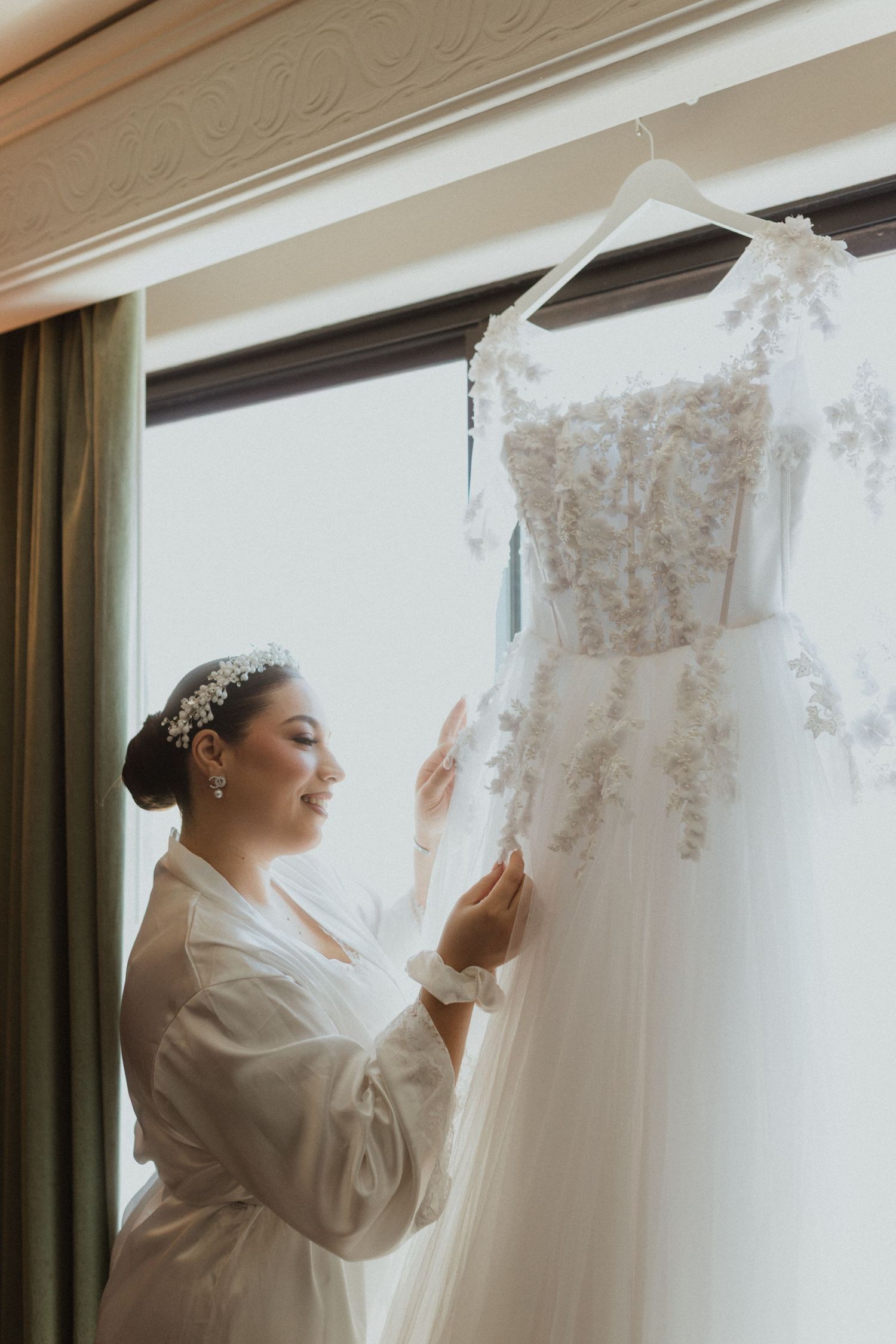 Wedding preparation scene with white gown hanging as person admires it.