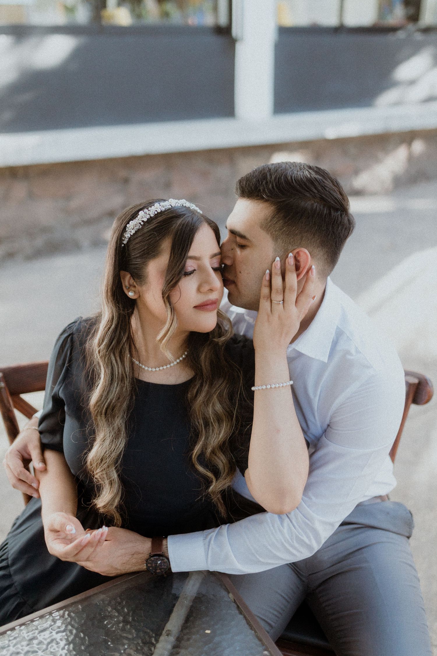 A romantic couple shares a tender kiss while sitting together on a bench.