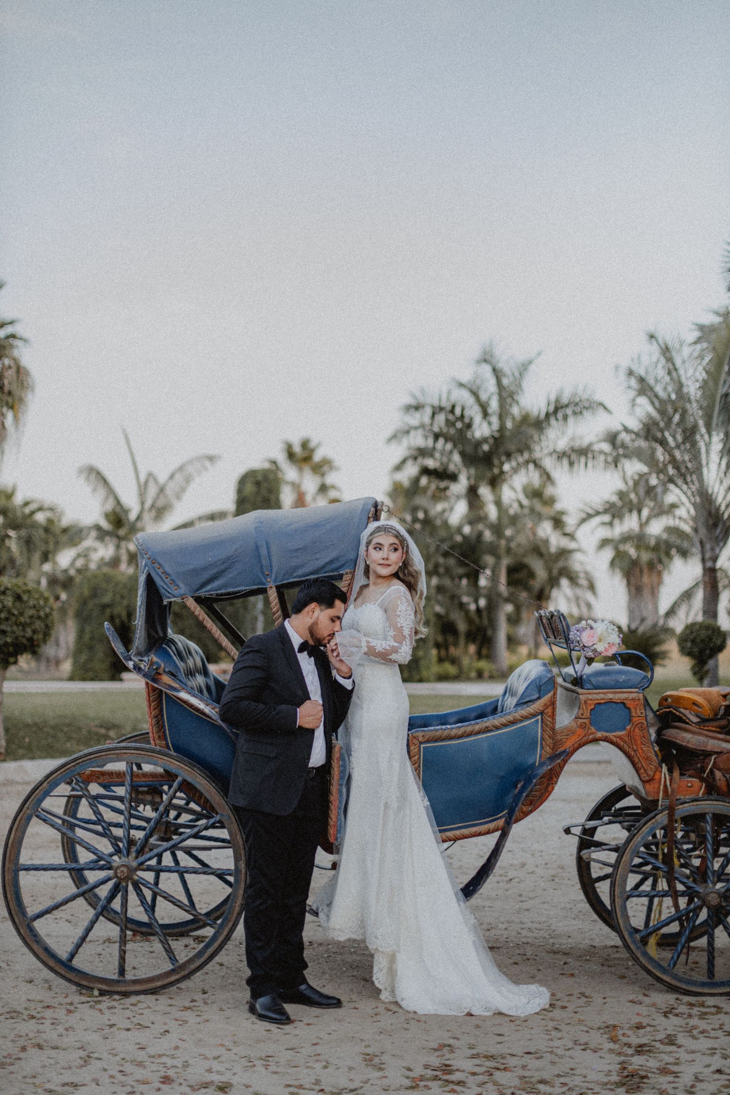 A couple poses with an ornate blue horse-drawn carriage during their wedding.
