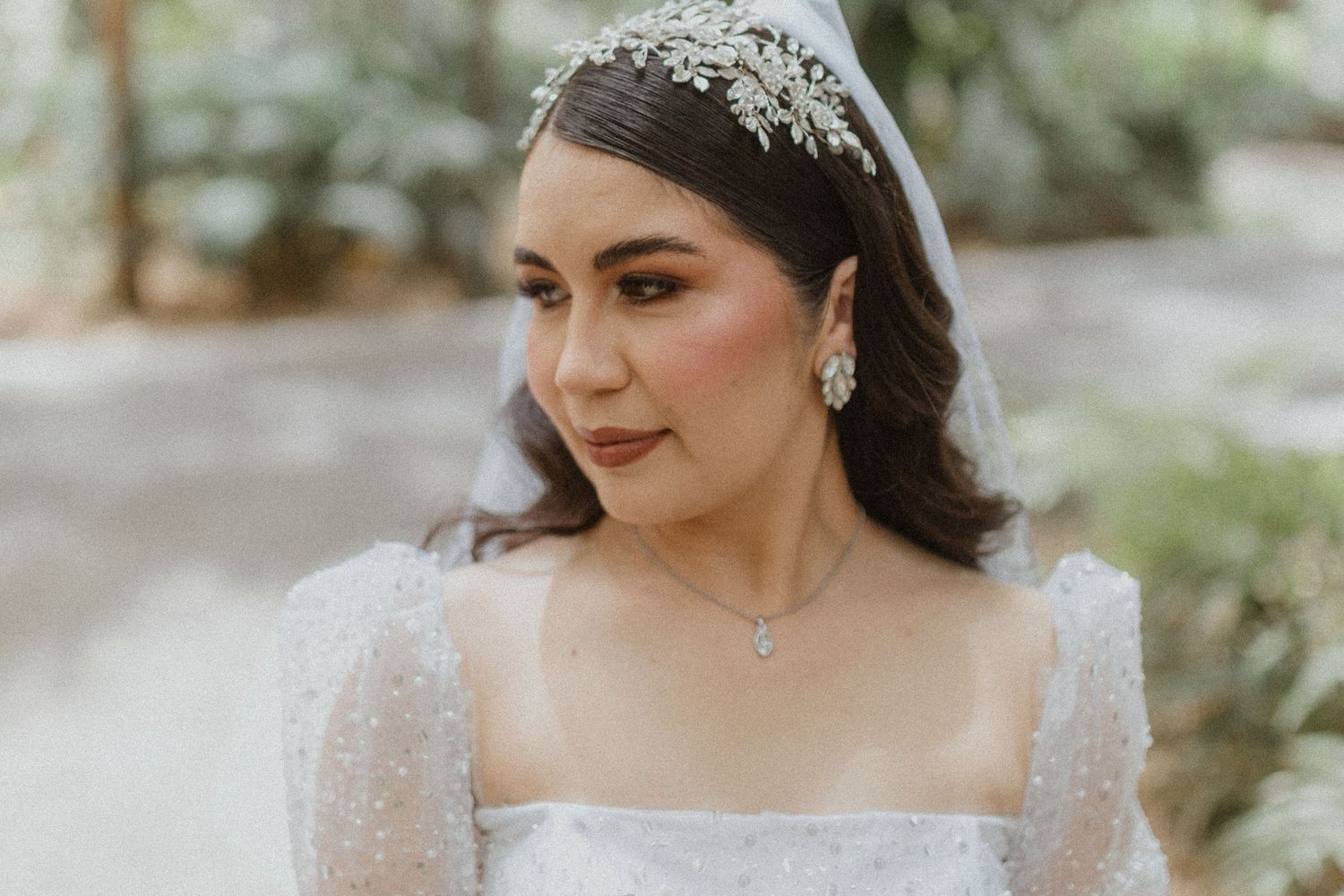 Bride in sparkling tiara and lace dress poses in natural light.