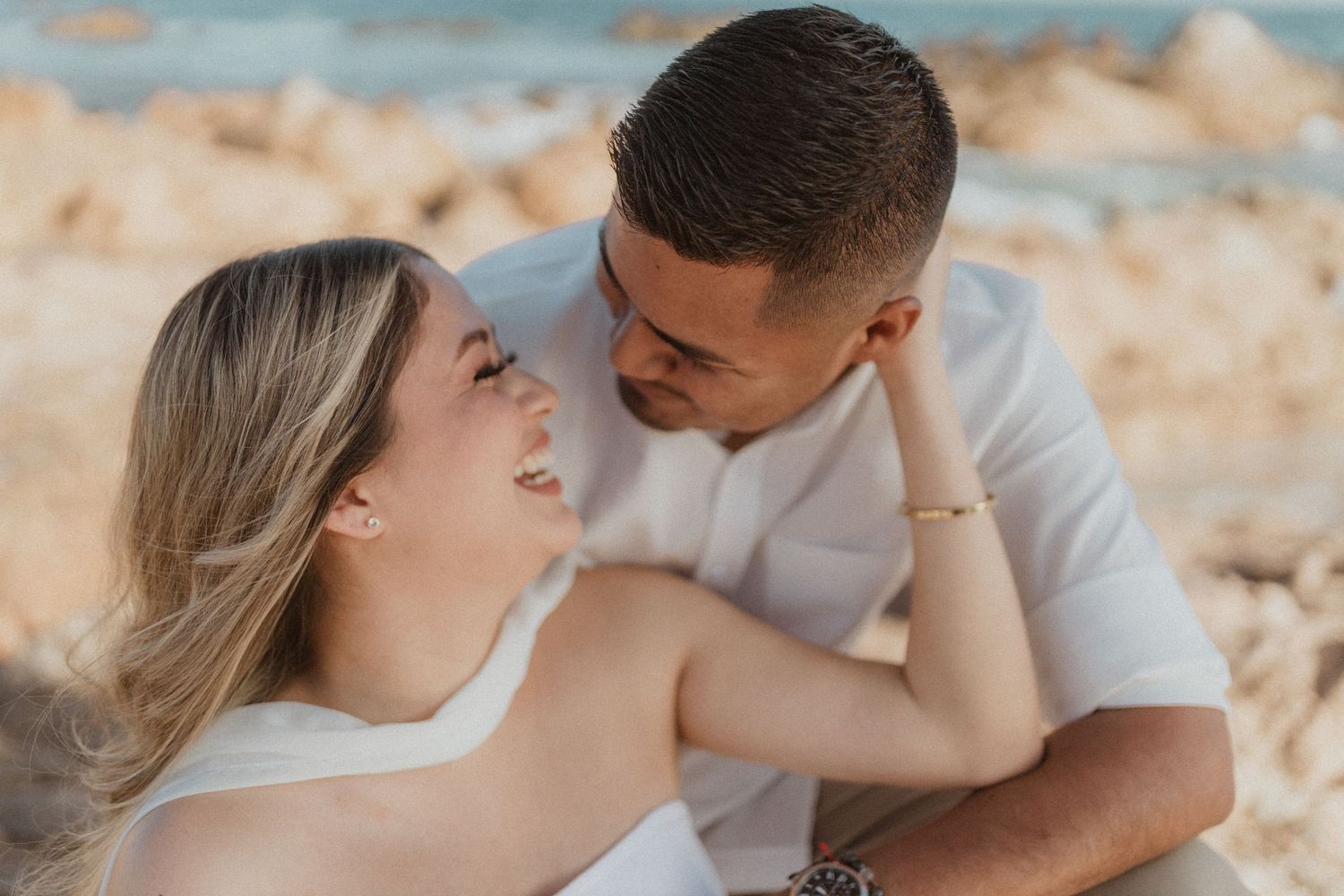 Couple wearing white outfits share intimate moments on sandy beach during golden hour.