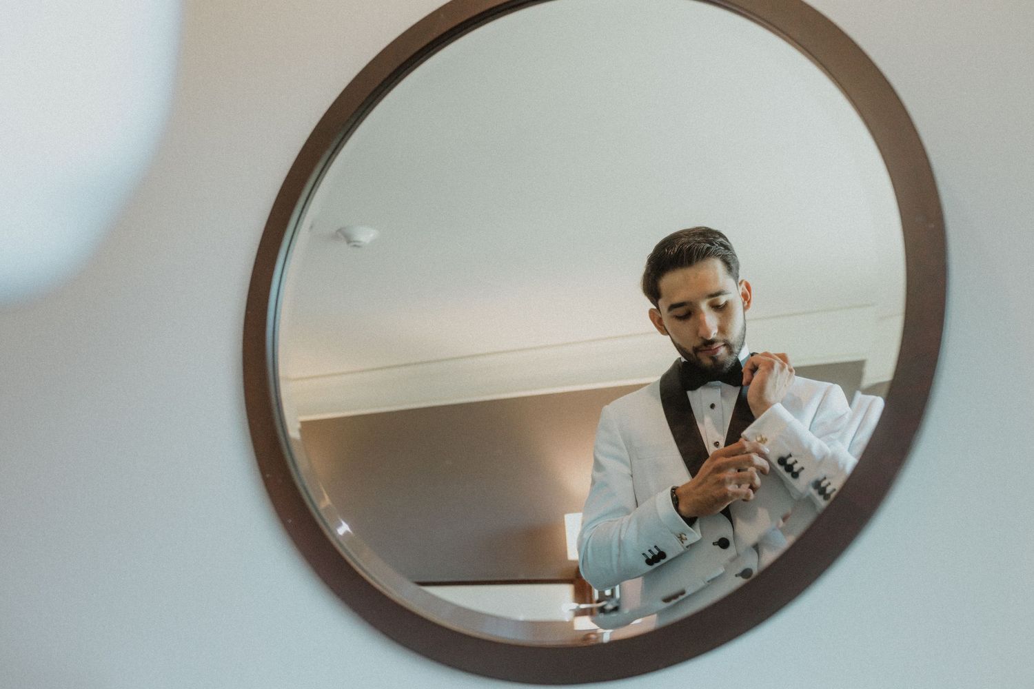 Reflection in circular mirror shows someone adjusting their bowtie.