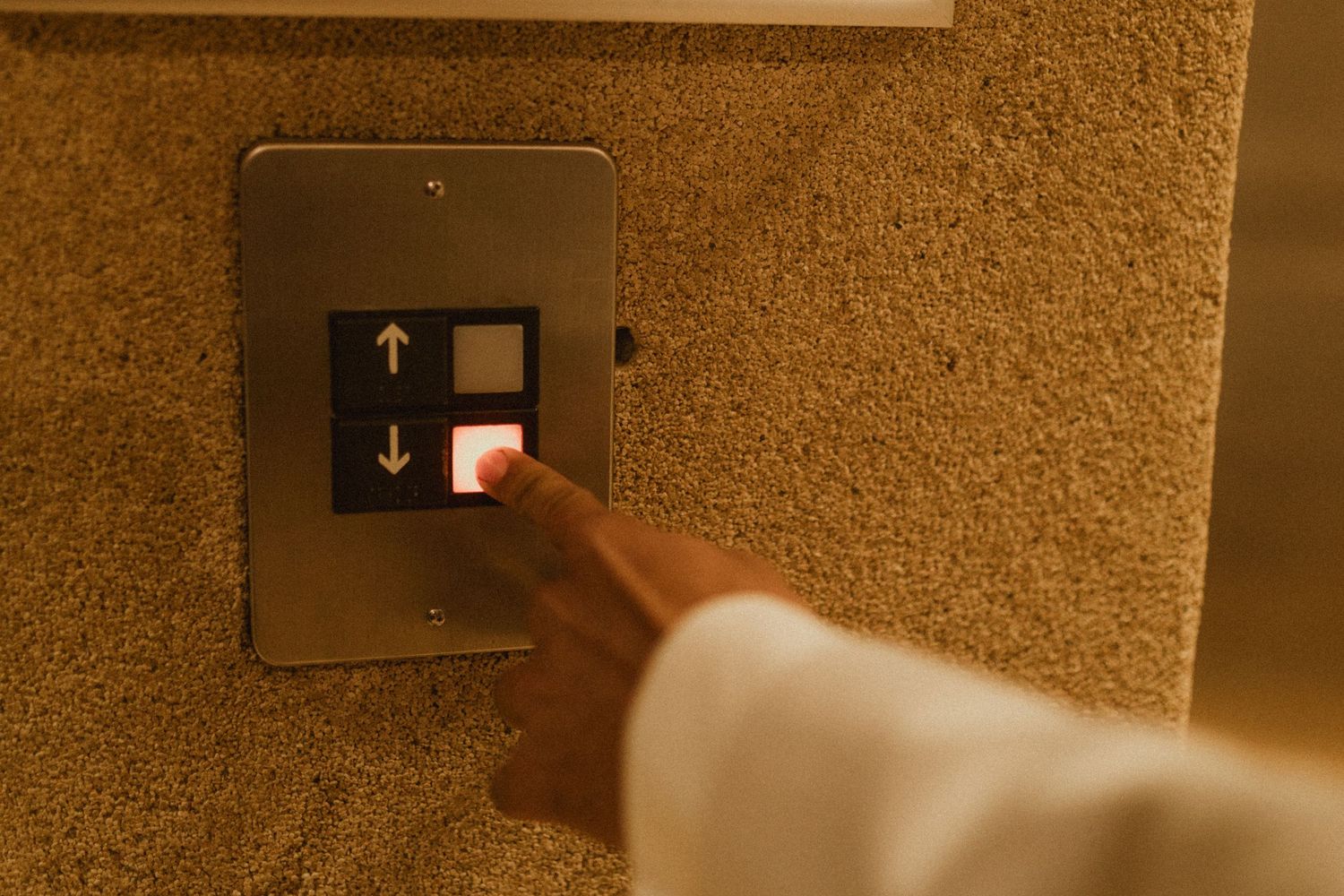 Hand pressing elevator button in hotel hallway.