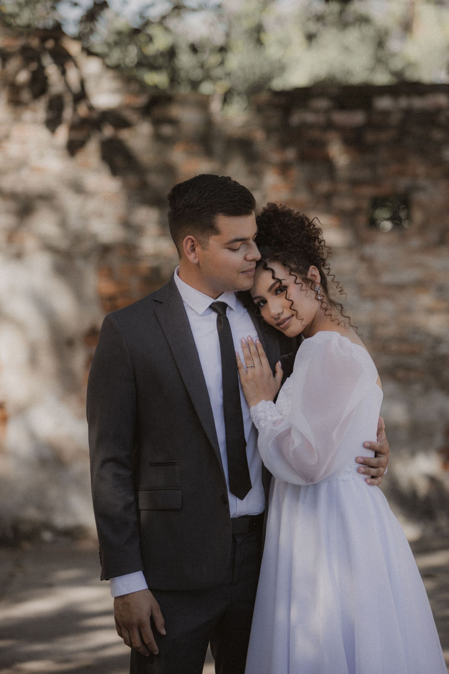 A romantic moment captured against a rustic brick wall backdrop.