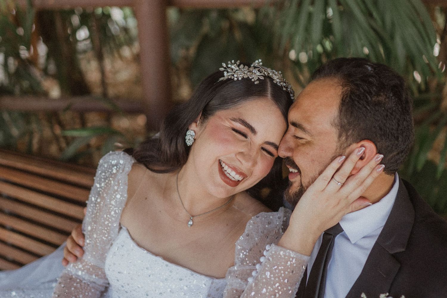 Couple shares joyful moment on wooden bench in garden setting.