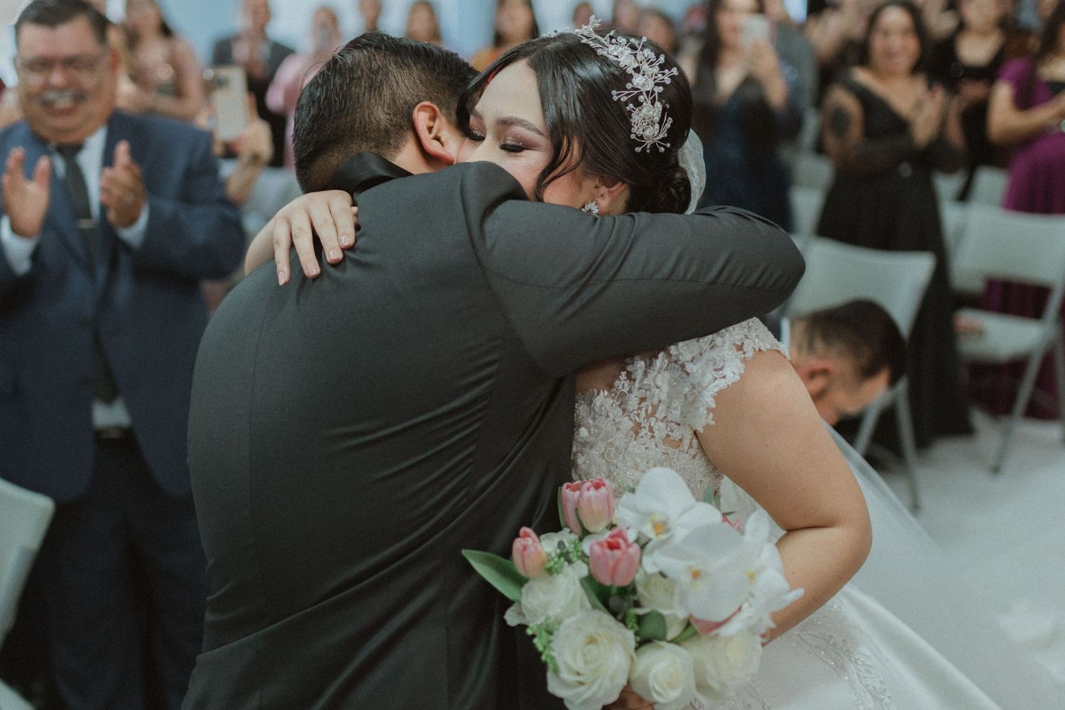 Emotional wedding ceremony moment with guests applauding in the background.