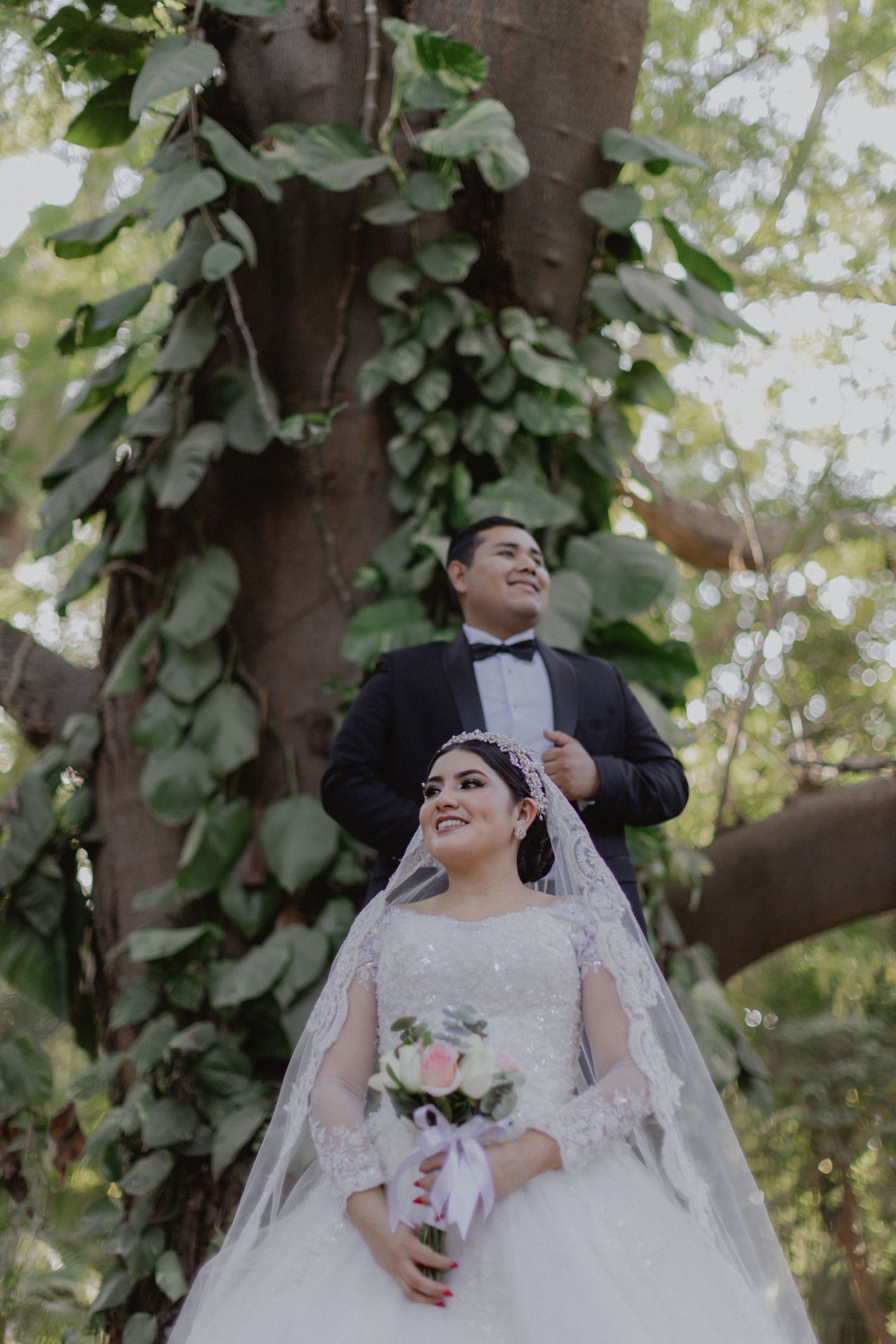 Wedding portrait under a tree with cascading vines and leaves creating natural backdrop.