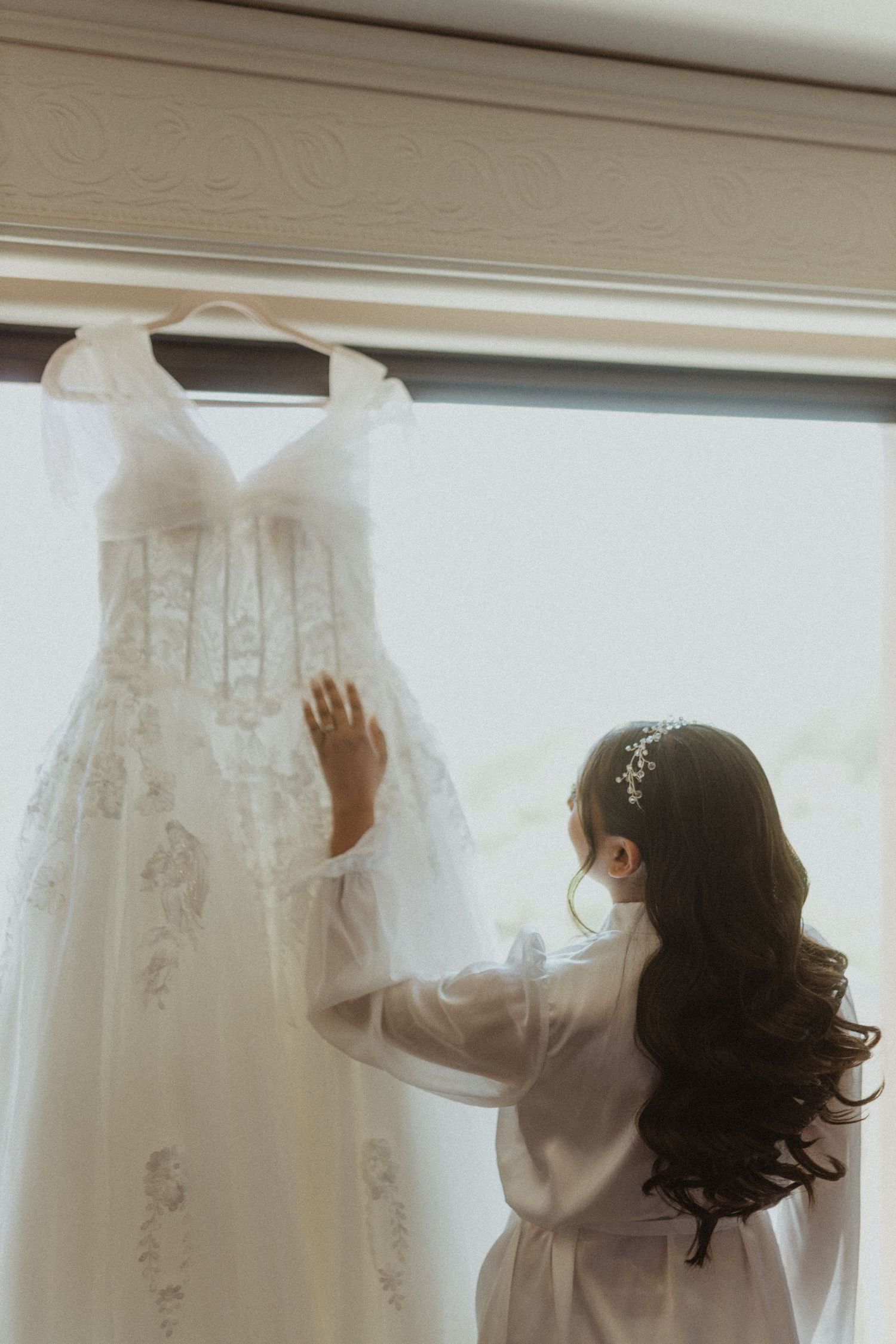 A sequence showing someone adjusting a white wedding dress hanging by a window.