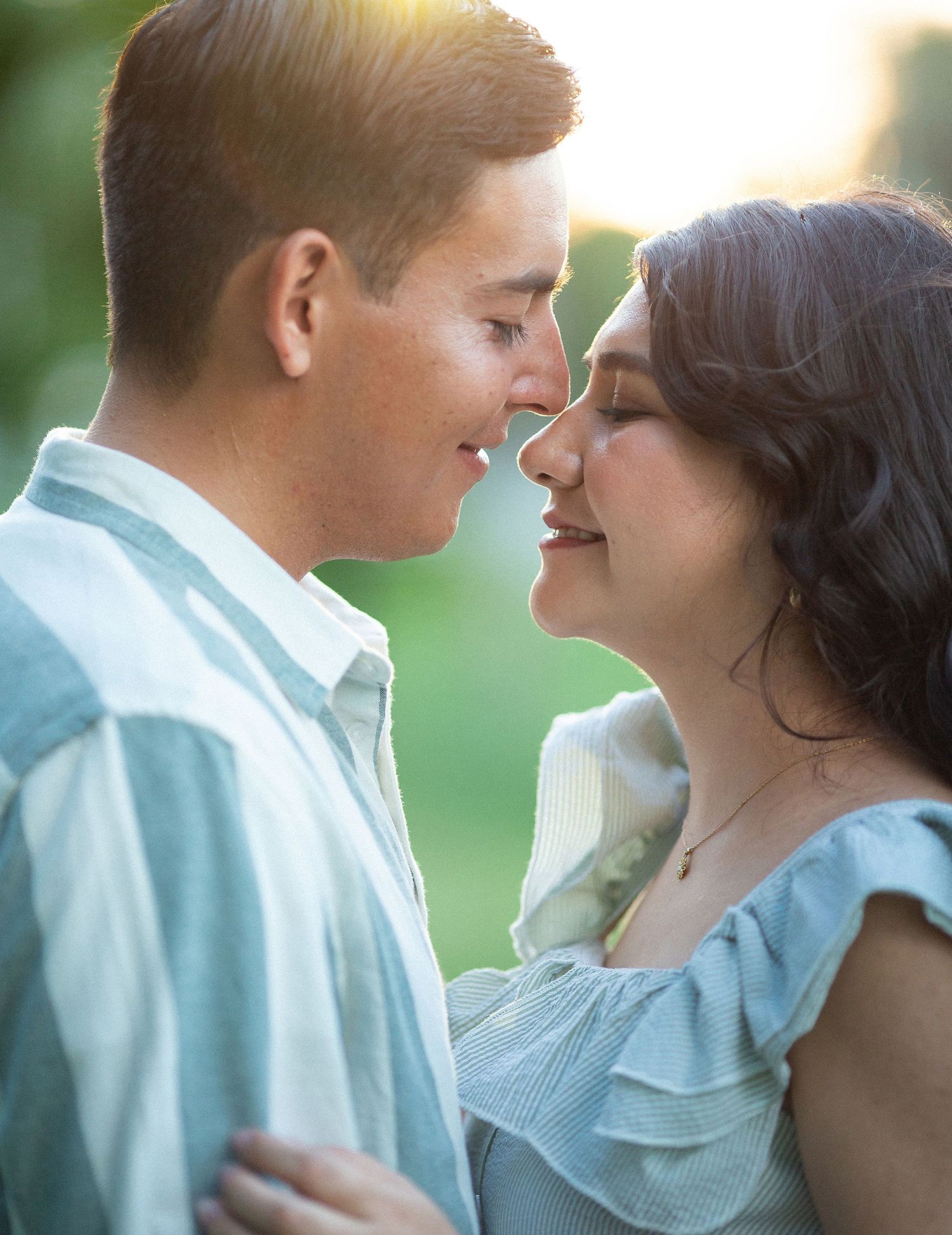 A romantic close-up of a couple in casual attire sharing a tender moment in golden sunlight.