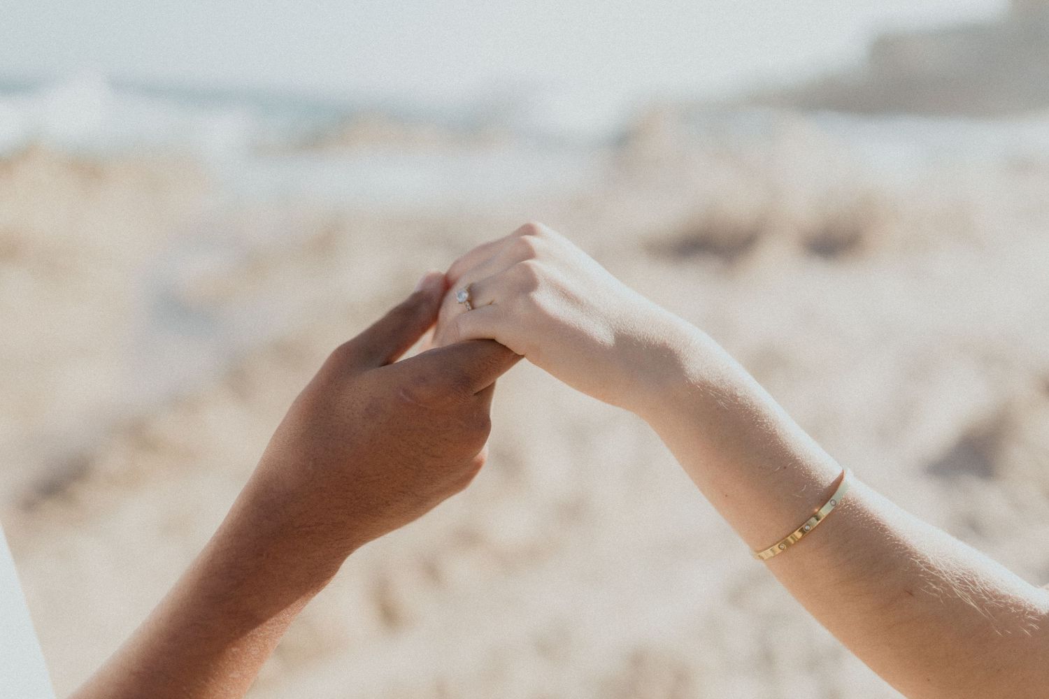 Close up of hands touching tenderly on sandy beach during sunset.