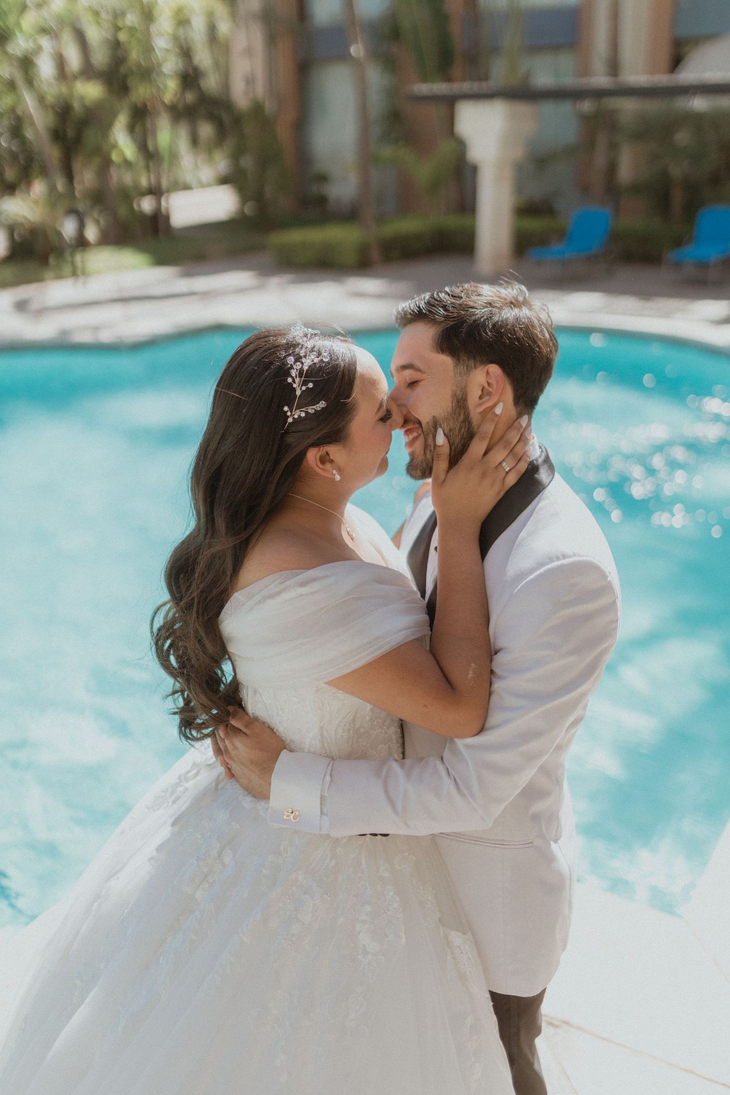 A romantic poolside wedding photo with the couple embracing in white attire.