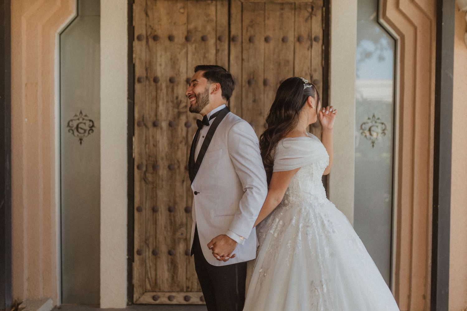A bride in a ballgown and groom in white tuxedo stand back to back during their wedding.