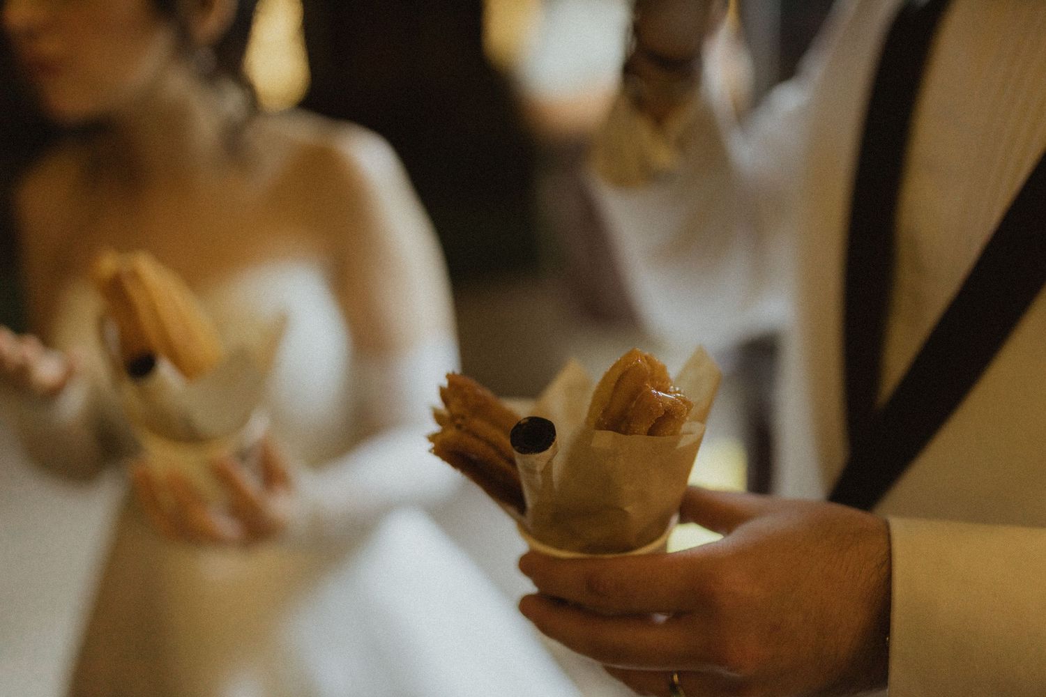 Close-up shot of hands holding churros at a wedding reception.