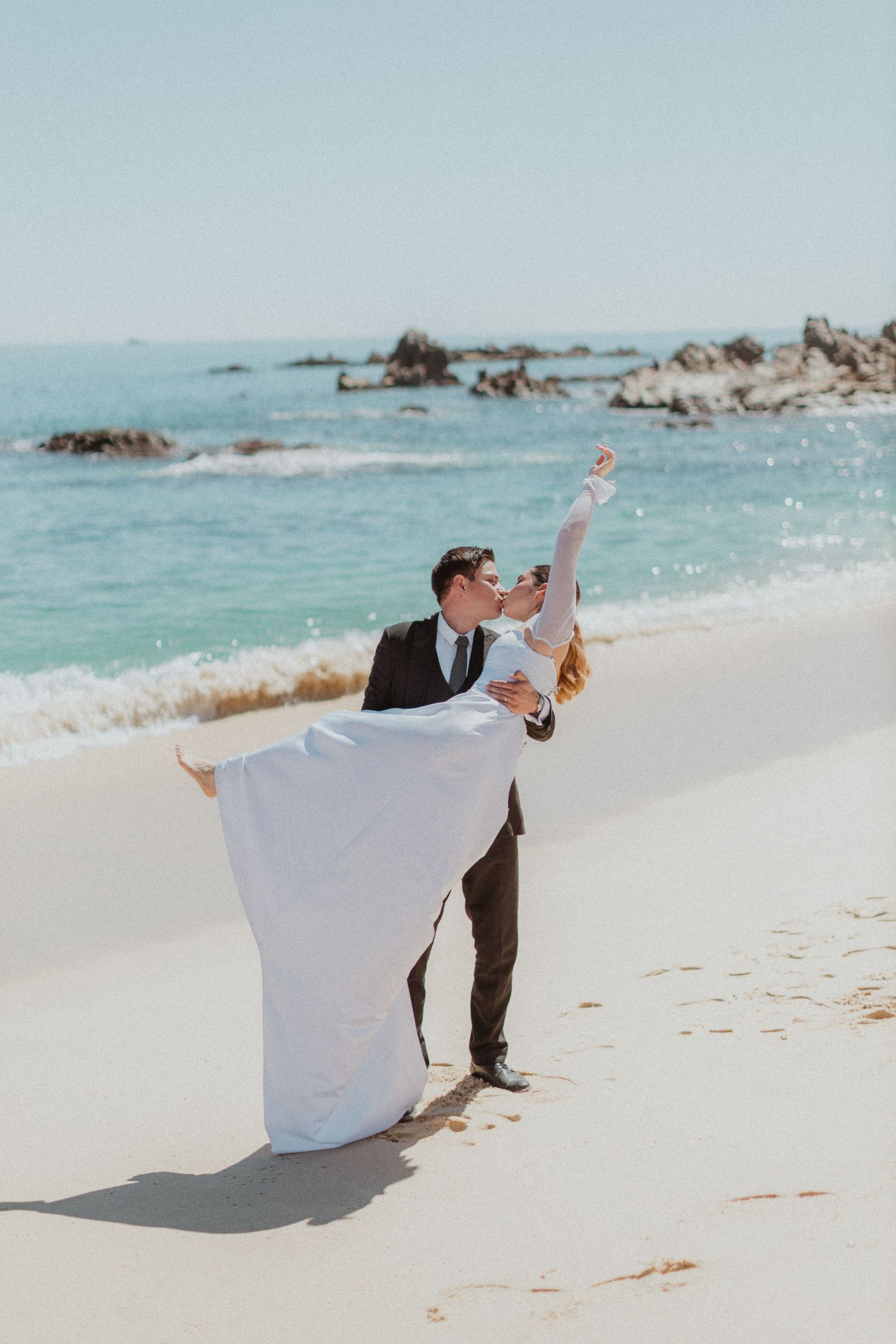 A dramatic beach wedding pose with the groom lifting the bride in her flowing white dress.