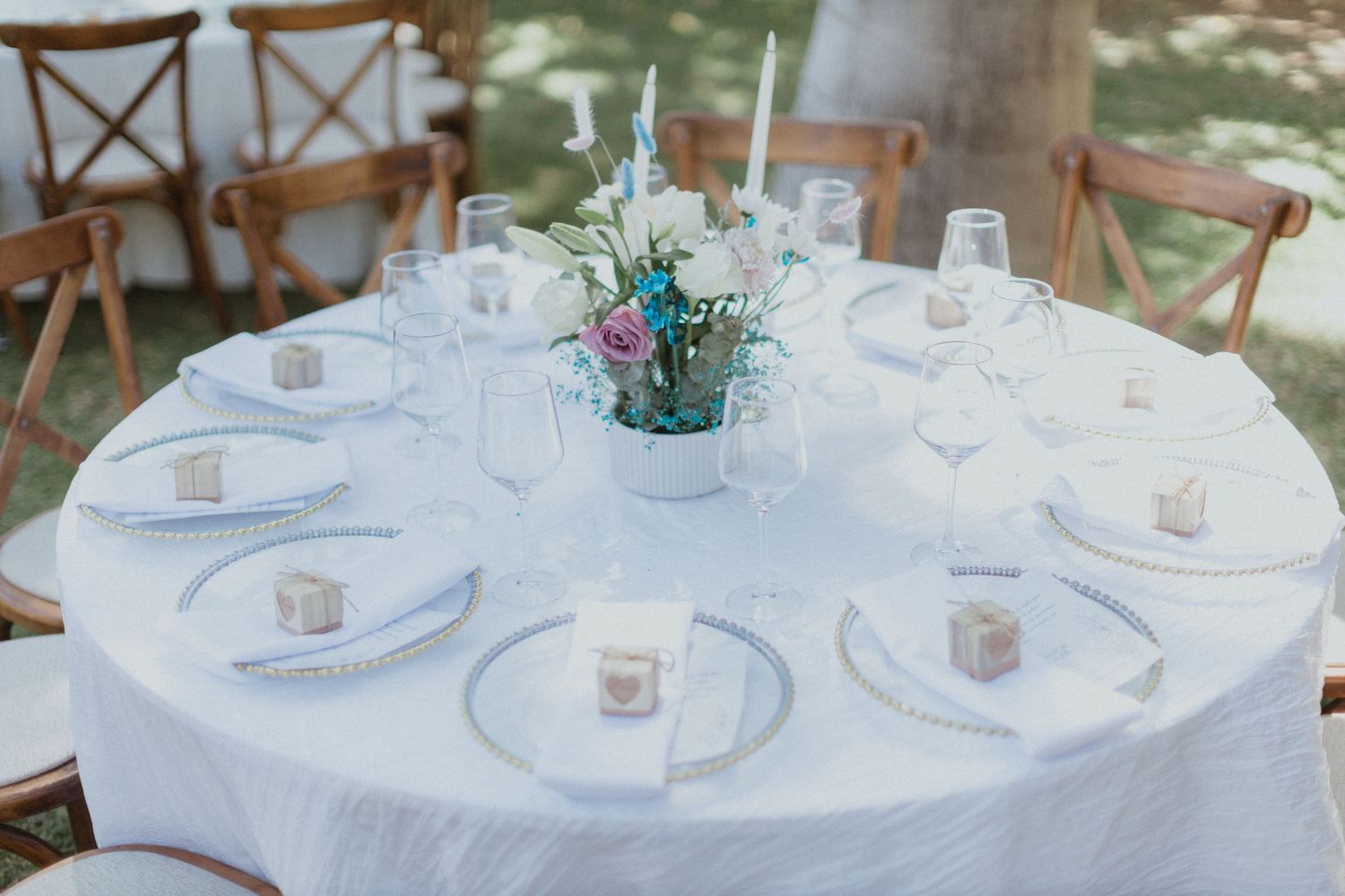 Elegant round table setting with white linens, fine china, and teal floral centerpiece.
