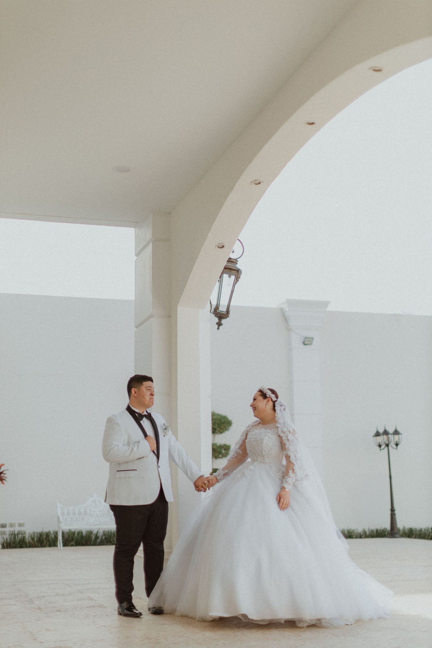 A wedding couple poses under an arched walkway with hanging lanterns.