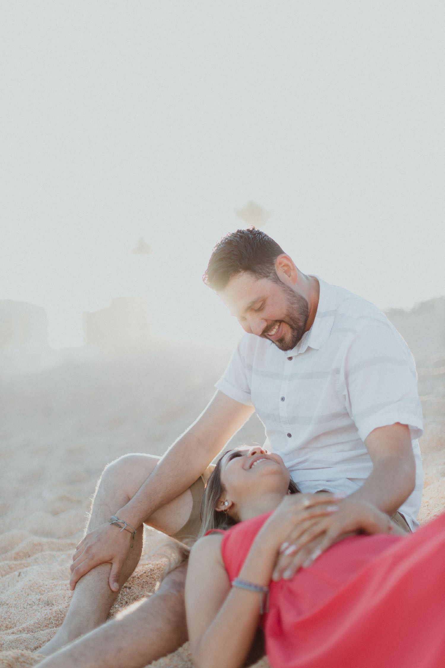 Relaxed couple lounges together on sandy beach during sunset photoshoot.