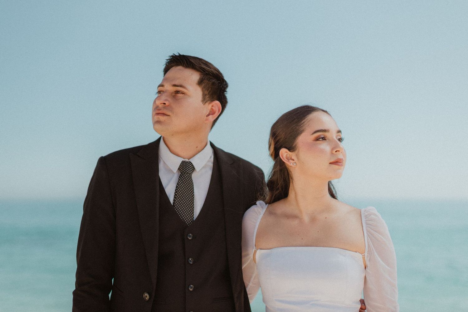 A elegant couple in wedding attire pose against the backdrop of a pristine beach.