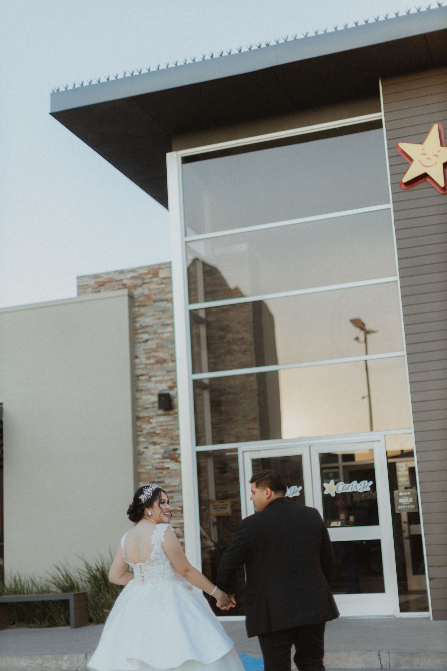 Bride and groom walking hand in hand towards modern building entrance with star decoration.