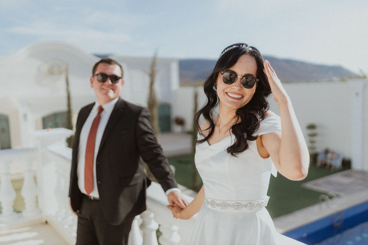 Elegant wedding couple with sunglasses walking along white Mediterranean balcony.